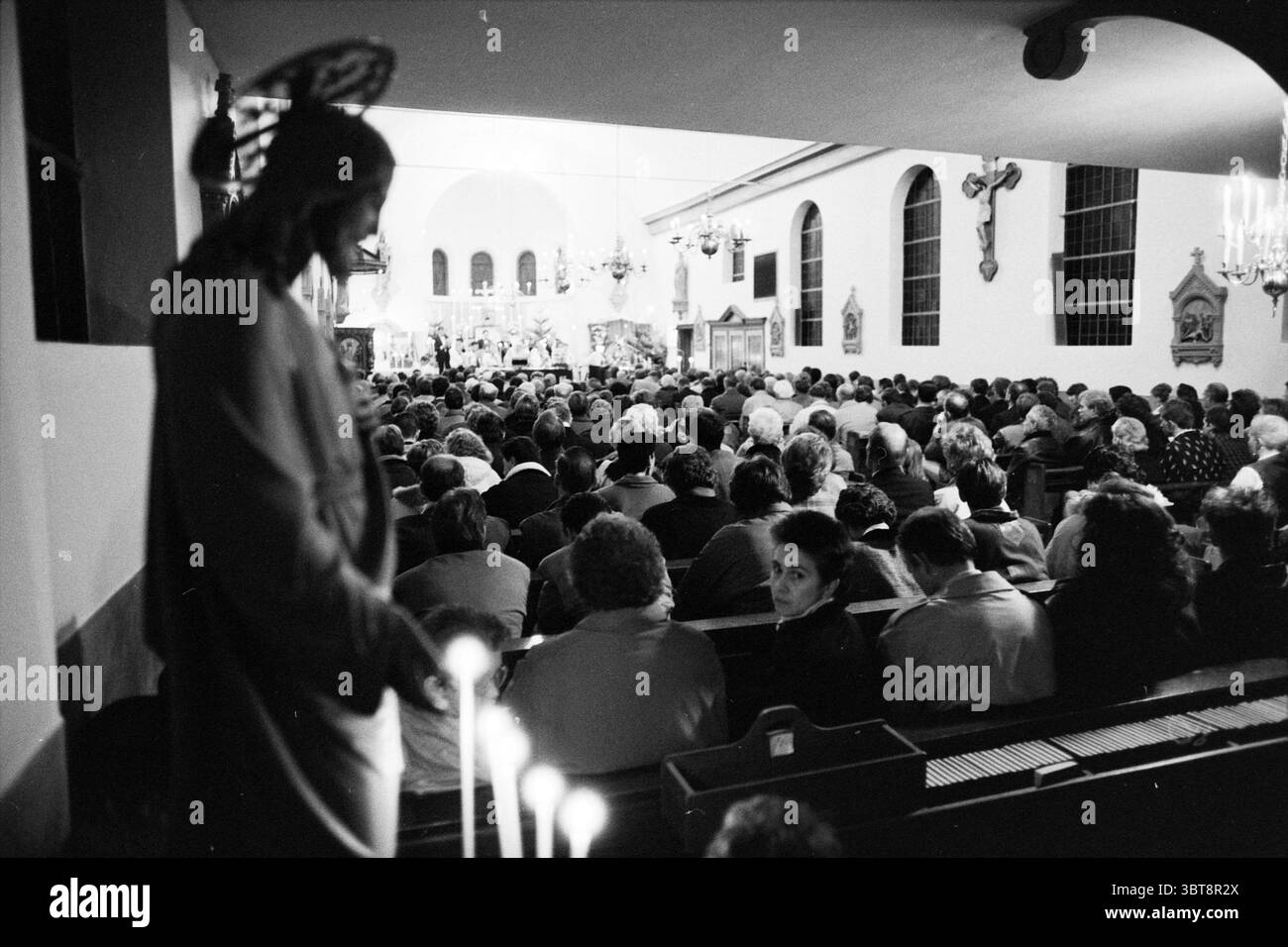 Service religieux RK Haarlemmerliede Churches, Whizgle News, Dutch Desk, pays-Bas, 1950 - 2000 on 24-12-1988. Voici les rubriques de l'image. La scène représente un intérieur bondé d'un lieu de culte, avec un nombre considérable de personnes rassemblées pour un service. L’atmosphère est solennelle et réfléchissante, amplifiée par un éclairage doux et chaleureux qui illumine doucement l’espace. À gauche, il y a une statue représentant une figure, probablement une icône religieuse, avec une expression sereine et des détails. La présence de la statue ancre la scène, contrastant avec la dynamique active Banque D'Images