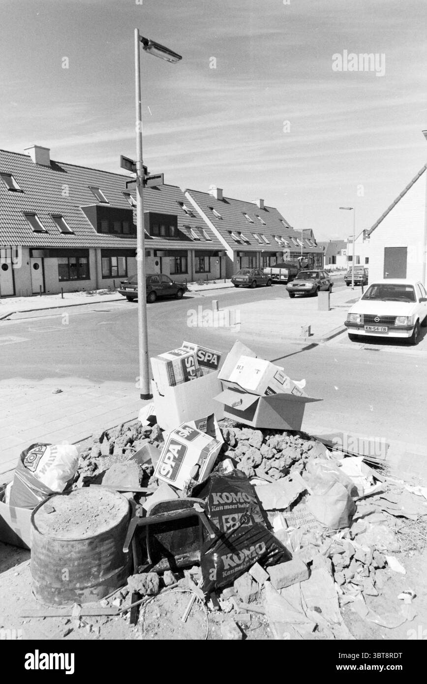 Déchets volumineux dans Overbos Garbage Hoofddorp Nederland, Whizgle News, Dutch Desk, pays-Bas, 1950 - 2000 le 03-08-1988. Ces rubriques sont illustrées dans l'image. La scène capture un coin de rue urbain caractérisé par un mélange de structures résidentielles et de désordre. D'un côté, les maisons soigneusement agencées avec des toits inclinés présentent un aspect uniforme ; leurs façades sont ornées de couleurs sourdes, principalement des nuances de gris et de beige. Chaque bâtiment a une allée ou une petite cour avant, contribuant à un sentiment de vie de banlieue. Au premier plan, un tas de débris perturbe l'atmos autrement ordonné Banque D'Images