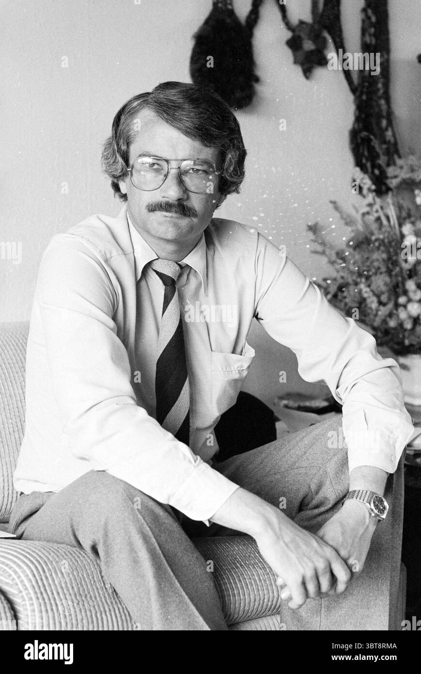 Michel Jager président de la VPRO et conseiller municipal de Heemstede pour D'66. Personnes. Télévision. Heemstede pays-Bas, Whizgle News, Dutch Desk, pays-Bas, 1950 - 2000 le 07-06-1980. L'image inclut ces rubriques. La scène montre un homme assis sur un canapé en tissu de couleur claire avec une posture détendue. Il a des cheveux courts et soignés et porte des lunettes qui complètent son comportement intelligent. Sa tenue se compose d'une chemise boutonnée, de couleur claire, et d'une cravate rayée affichant un mélange de tons discrets, ajoutant une touche formelle à son apparence générale. Il associe ceci avec Banque D'Images