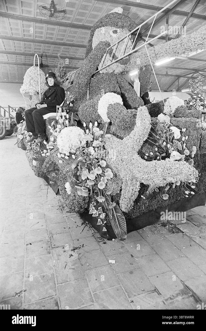 Parade flotte dans Hobaho halls lisse Flower exposition de fleurs Parade, Whizgle News, Dutch Desk, pays-Bas, 1950 - 2000 le 24-04-1976. Ce sont les éléments de l'image. La scène dispose d'un grand flotteur décoré abondamment avec un éventail de fleurs colorées, créant un affichage vif et complexe. Complétant les éléments floraux, le flotteur a principalement la forme d'une figure animale, qui est conçue de manière stylisée, mettant en valeur le savoir-faire impliqué dans l'arrangement floral. Assis au sommet du flotteur est un individu vêtu d'une tenue sombre, paraissant calme et composé au milieu du live Banque D'Images