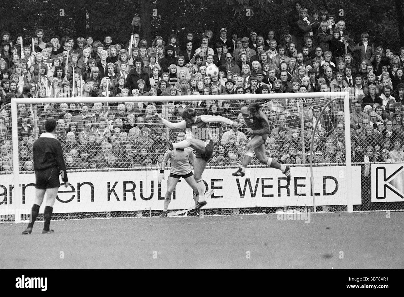 Match de football Ajax - AZ ?., Whizgle News, Dutch Desk, pays-Bas, 1950 - 2000. Ce sont les éléments de l'image. Dans une scène sportive dynamique, les joueurs s’engagent dans un moment d’action intense sur un terrain de football. Le cadre est vibrant, bourdonnant d'énergie alors qu'une foule nombreuse se rassemble en arrière-plan, composée de spectateurs enthousiastes. Ils sont vêtus d'un mélange de vêtements décontractés, certains portant des foulards et des maillots, montrant leur soutien à leurs équipes. Le champ est d'un vert riche, contrastant avec les lignes blanches marquées du terrain. Au premier plan, un gardien de but s'accroupit Banque D'Images