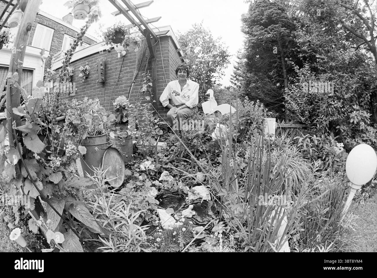 Femme posant dans (propre ?) Garden, Whizgle News, Dutch Desk, pays-Bas, 1950 - 2000 en 1993. L'image contient ces rubriques. La scène capture un jardin luxuriant regorgeant de plantes et de fleurs diverses. La verdure semble vibrante, avec différentes nuances de vert dominant le feuillage. Les fleurs colorées ajoutent des éclaboussures de couleur, mettant en valeur des teintes de jaune, rose, violet et blanc. Au milieu de ce cadre verdoyant se trouve une personne, vêtue d'une tenue de couleur claire qui contraste doucement avec la verdure. Leur expression semble calme et contemplative, suggérant un moment paisible passé Banque D'Images