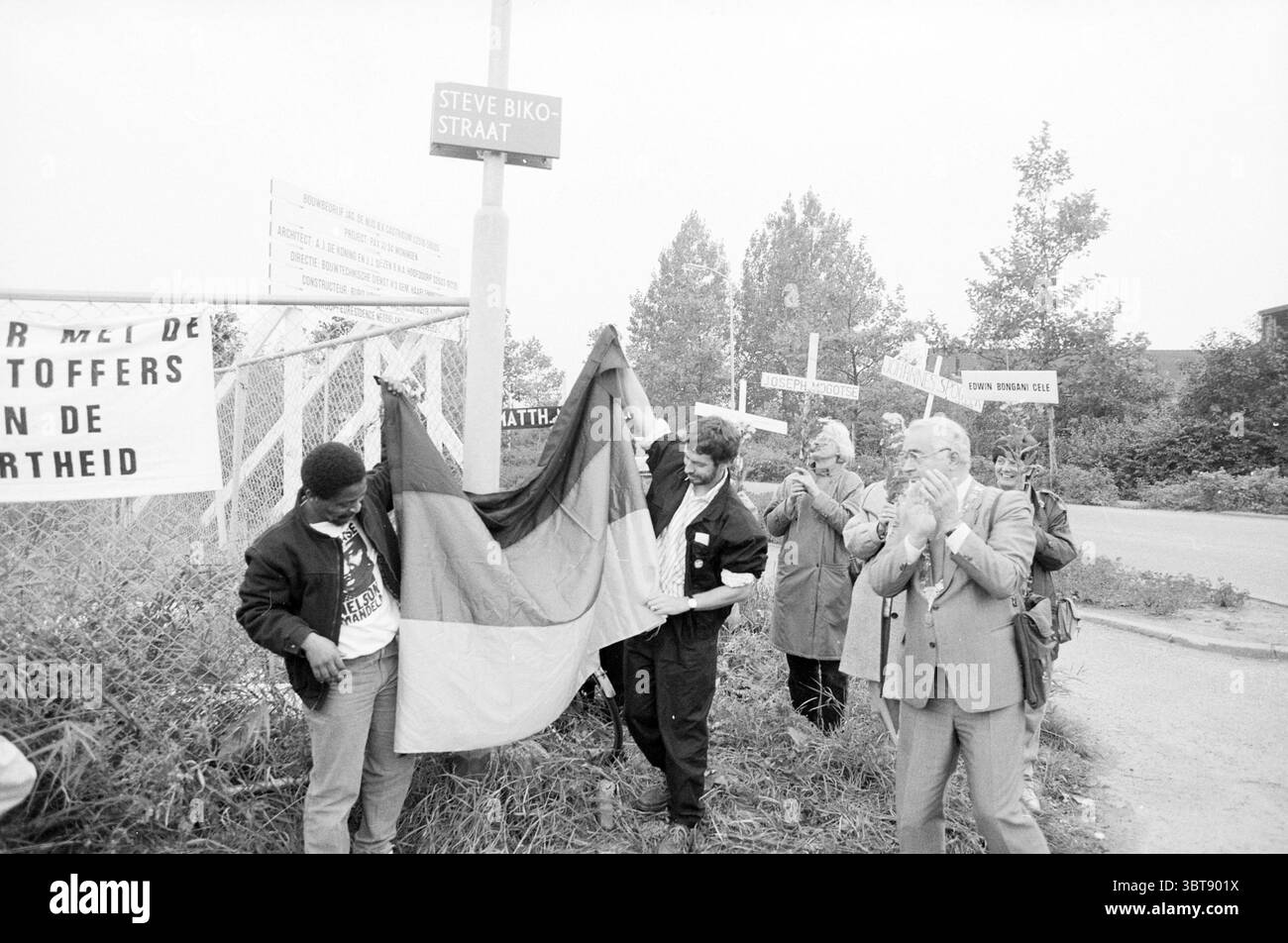 Révélation du nom de rue Steve Bike par Mesman H'dorp dévoilement Hoofddorp Steve Bikostraat pays-Bas, Whizgle News, Dutch Desk, pays-Bas, 1950 - 2000 on 11-10-1987. L'image inclut ces rubriques. La scène capte un moment d’importance, centré autour d’un drapeau qui est en train d’être dévoilé. Un groupe de personnes se réunit près d'un panneau indiquant que l'emplacement est une rue ou un espace public. L'atmosphère semble sombre mais pleine d'espoir, reflétant un moment de souvenir ou de célébration. Au premier plan, quelques personnes participent activement à l'événement. Une personne est dans l'AC Banque D'Images