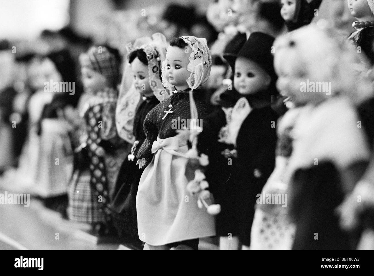 Musée de la marionnette Amstelveen Musée musées poupées spectacles de marionnettes spectacles de marionnettes théâtre de marionnettes Amstelveen, Whizgle News, Dutch Desk, pays-Bas, 1950 - 2000 on 20-11-1979. L'image contient ces rubriques. La scène présente une longue rangée de poupées, alignées méticuleusement. Chaque poupée présente une tenue unique, reflétant différents styles et peut-être des influences culturelles. Les vêtements vont de robes traditionnelles ornées de dentelle et de broderie à des vêtements plus modernes, indiquant une variété de contextes historiques ou de représentations thématiques. Les poupées elles-mêmes ont des expressions faciales distinctes, certaines app Banque D'Images