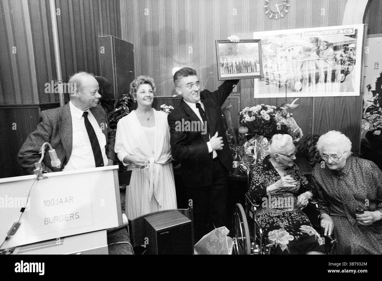 100 ans d'existence du café d'examen de conduite Zocherstraat. Anniversaires du Jubilé Haarlem Zocherstraat pays-Bas, Whizgle News, Dutch Desk, pays-Bas, 1950 - 2000 on 02-11-1986. L'image montre ces rubriques. La scène capture un rassemblement animé à l'intérieur, caractérisé par une atmosphère chaleureuse et festive. La chambre dispose de lambris en bois, créant un fond riche et texturé qui renforce le sentiment de nostalgie. Au premier plan, quatre individus sont positionnés en demi-cercle, dégageant un mélange d'excitation et de fierté. À gauche, un homme avec une tête chauve brillante et portant un costume sombre s. Banque D'Images