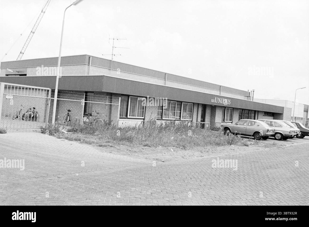 Ext. Unievis IJmuiden bâtiments extérieurs Velsen - IJmuiden pêche et autres poissonniers pêchant IJmuiden pays-Bas, Whizgle News, Dutch Desk, pays-Bas, 1950 - 2000 on 10-08-1979. L'image contient ces rubriques. La scène représente un modeste bâtiment industriel caractérisé par un style architectural simple, avec un toit plat et une orientation horizontale. La façade est principalement composée d'un mélange de briques et de panneaux métalliques, avec des sections alternées de tons clairs et sombres créant du contraste. Les fenêtres bordent l'avant, permettant des aperçus de l'intérieur, qui semble h Banque D'Images