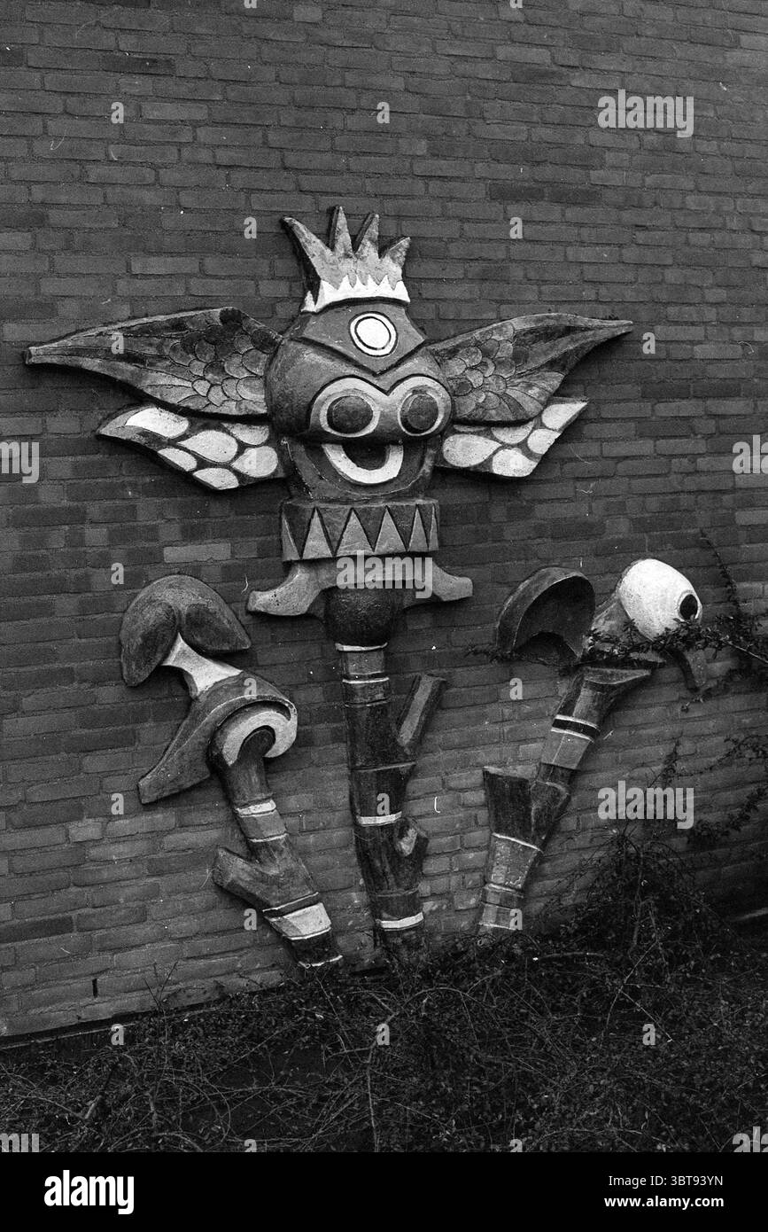 Peinture murale jardin d'enfants 'Gnomes'. Peinture murale, Whizgle News, Dutch Desk, pays-Bas, 1950 - 2000 sur 12-12-1973. L'image montre ces rubriques. La scène représente une murale vibrante montée sur un mur de briques texturées. La murale présente un caractère imaginatif qui combine des éléments d'une créature et d'une fleur. Cette figure a une tête circulaire ornée d'une couronne et de verres circulaires surdimensionnés qui lui confèrent une personnalité fantaisiste. Sa bouche est large et expressive, ressemblant à un sourire qui ajoute un ton ludique. La créature est flanquée de deux fleurs stylisées, chacune avec des tiges allongées qui plongent Banque D'Images