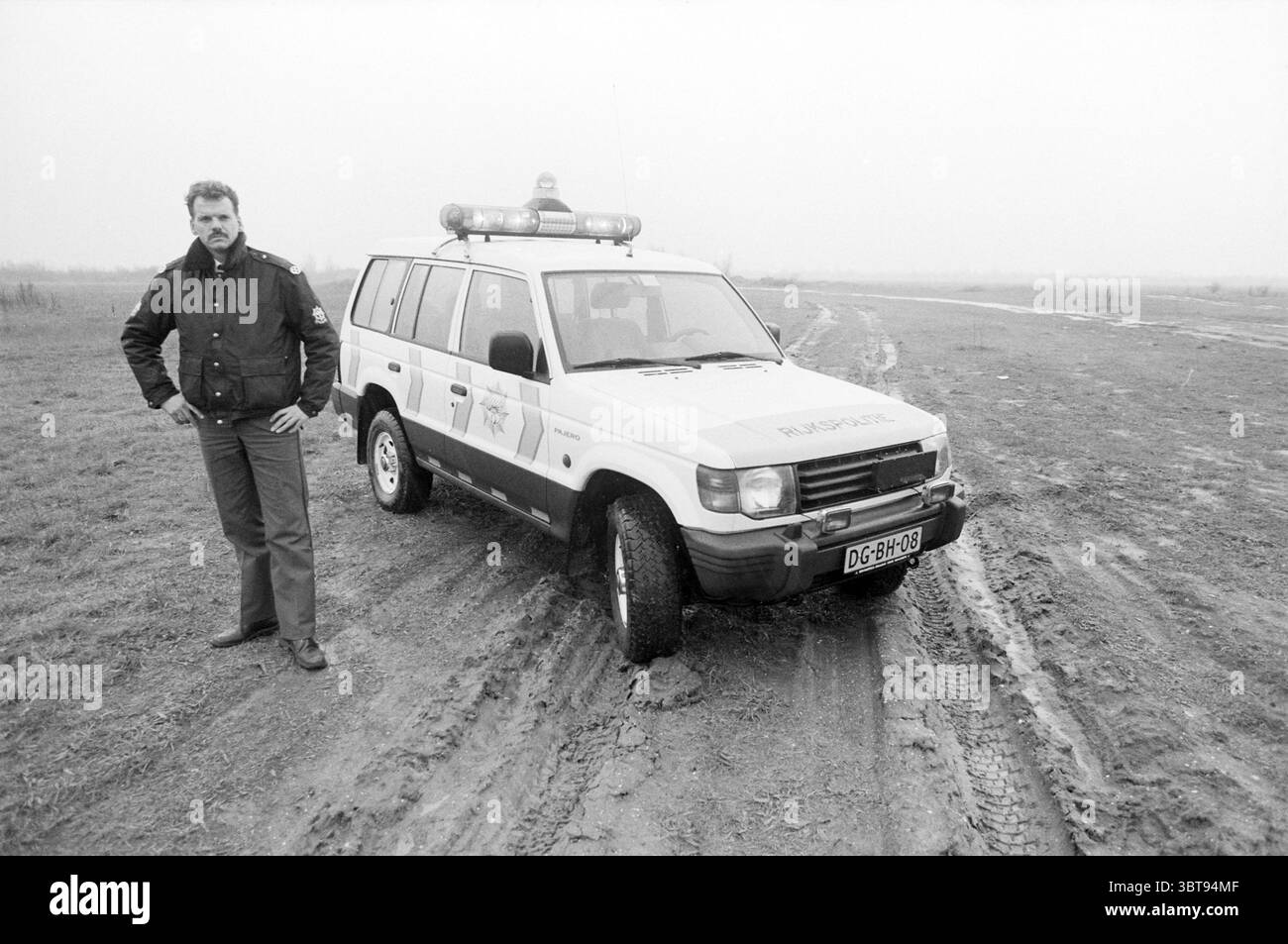 New jeep Halfweg police Halfweg, Whizgle News, Dutch Desk, pays-Bas, 1950 - 2000 le 17-11-1991. Ces rubriques sont illustrées dans l'image. Dans la scène, un homme se tient confiant à côté d'un véhicule hors route robuste. Le véhicule est principalement peint dans une couleur claire, avec des marques distinctes qui suggèrent qu'il appartient à une organisation de service ou d'urgence, y compris une barre lumineuse brillante sur le toit. L'homme est habillé d'une veste sombre, peut-être un uniforme, avec une coupe structurée qui transmet l'autorité. Il a une expression sérieuse, projetant un sens du devoir et de la concentration. Sa position est solide, avec une Banque D'Images