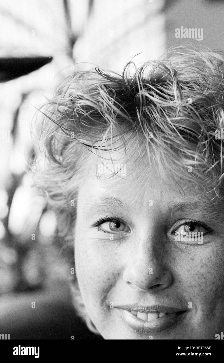 V.D. Lee cycliste, Whizgle News, Dutch Desk, pays-Bas, 1950 - 2000 le 07-08-1996. Ces rubriques sont illustrées dans l'image. La scène met en scène un jeune individu avec des cheveux de couleur claire frappés dans des boucles douces et ludiques qui encadrent leur visage. Leur peau a un ton naturel et sain orné d'une dispersion de taches de rousseur, donnant un air de dynamisme jeune. Les yeux de la personne sont brillants et expressifs, capturant un sentiment de chaleur et de convivialité. En arrière-plan, il y a des notes d'un environnement vivant, avec des formes abstraites et des jeux de lumière suggérant les contours de plantes ou de pelage mou Banque D'Images