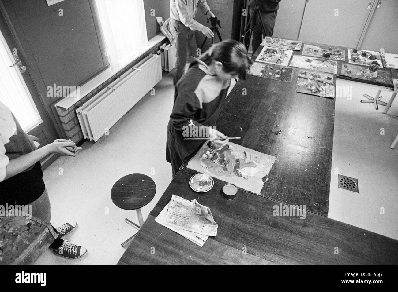 Painting Howler Buoy, Whizgle News, Dutch Desk, pays-Bas, 1950 - 2000 sur 27-02-1994. L'image contient ces rubriques. La scène se déroule dans un studio d'art très éclairé, caractérisé par de grandes fenêtres qui permettent à la lumière naturelle de baigner la pièce dans une douce lueur. Les murs sont ornés de diverses œuvres d'art, faisant allusion à la créativité et aux projets en cours. Une longue table en bois occupe le devant de la scène, parsemée de palettes enduites de couleurs vives, mélangeant des nuances de rouge, bleu, jaune et vert. Les pinceaux reposent dans des pots, et il y a un petit plat en céramique rempli de différentes teintes de peinture, Banque D'Images