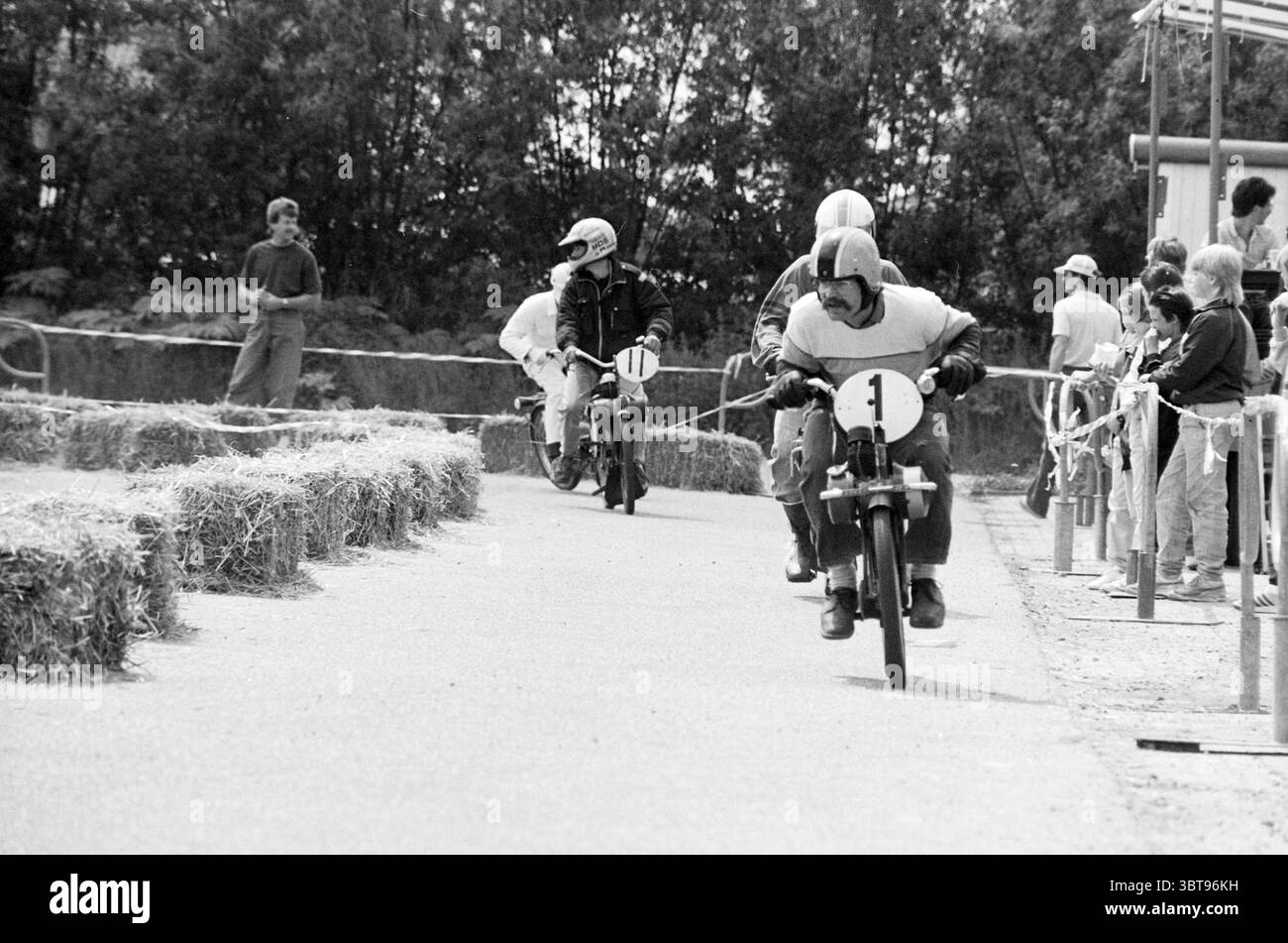 Solex race Rijsenhout cyclomoteurs riders cyclomoteurs Rijsenhout, Whizgle News, Dutch Desk, The Netherlands, 1950 - 2000 sur 14-06-1987. Ces rubriques sont illustrées dans l'image. La scène capture une course de Go-kart énergique se déroulant dans un lieu extérieur entouré d'une végétation luxuriante. Au premier plan, deux coureurs sur de petits karts roulent sur un chemin droit. Le premier pilote, portant un casque au design orange vif, se penche en avant, montrant sa détermination à accélérer. Son Go-kart est peint dans un style de course classique, orné d'un chiffre audacieux '1' sur le côté. Le deuxième coureur suit de près Banque D'Images