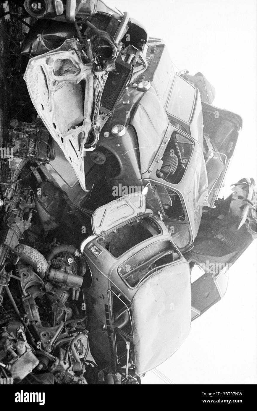 Junkyard, Whizgle News, Dutch Desk, pays-Bas, 1950 - 2000 sur 01-1981. L'image inclut ces rubriques. La scène présente une pile dense de véhicules abandonnés, créant un paysage chaotique et industriel. Les voitures sont mélangées, avec certains renversés, leurs roues exposées et le métal rouillé scintiller durement dans la lumière. Différentes nuances de gris et de noir dominent la composition, entrecoupées de notes de couleurs délavées provenant des anciens travaux de peinture, tels que des restes de bleu, rouge et vert. Le cadre semble être un terrain à la casse, où les véhicules sont laissés à la décomposition sous le ciel ouvert. L'atmosphe Banque D'Images