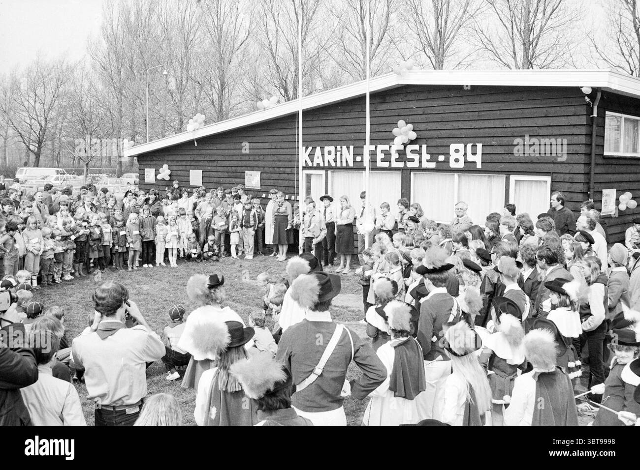 Ouverture du clubhouse Padvinders Vondelweg ouvertures mises en service Haarlem Vondelweg pays-Bas, Whizgle News, Dutch Desk, pays-Bas, 1950 - 2000 le 15-04-1984. Voici les rubriques de l'image. La scène capture un rassemblement animé en plein air devant un grand bâtiment en bois, caractérisé par un extérieur brun foncé. Cette structure a de grandes fenêtres et un toit simple, lui donnant un aspect rustique. Devant le bâtiment, une foule diversifiée de personnes, y compris de nombreux enfants vêtus de costumes colorés, est Assemblée. L’ambiance est festive, avec des ballons à l’ombre vibrante Banque D'Images