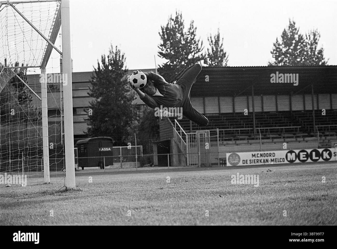 Rob Boersma H.F.C. Haarlem Football Haarlem, Whizgle News, Dutch Desk, pays-Bas, 1950 - 2000 on 10-09-1974. Ce sont les éléments de l'image. Une scène se déroule sur un terrain de football herbeux, dominé par un grand poteau de but à gauche. La toile de fond présente des sièges surélevés, probablement une petite tribune, faisant allusion à un match en cours ou à une séance d'entraînement. De grands arbres bordent le périmètre, leurs feuilles légèrement perturbées par une douce brise, contribuant à l'atmosphère tranquille. Un joueur, capturé en plein air, saute vers le but, les yeux se concentrent intensément sur le ballon de football noir et blanc juste un Banque D'Images Rob Boersma H.F.C. Haarlem Football Haarlem, Whizgle News, Dutch Desk, pays-Bas, 1950 - 2000 on 10-09-1974. Ce sont les éléments de l'image. Une scène se déroule sur un terrain de football herbeux, dominé par un grand poteau de but à gauche. La toile de fond présente des sièges surélevés, probablement une petite tribune, faisant allusion à un match en cours ou à une séance d'entraînement. De grands arbres bordent le périmètre, leurs feuilles légèrement perturbées par une douce brise, contribuant à l'atmosphère tranquille. Un joueur, capturé en plein air, saute vers le but, les yeux se concentrent intensément sur le ballon de football noir et blanc juste un Banque D'Images