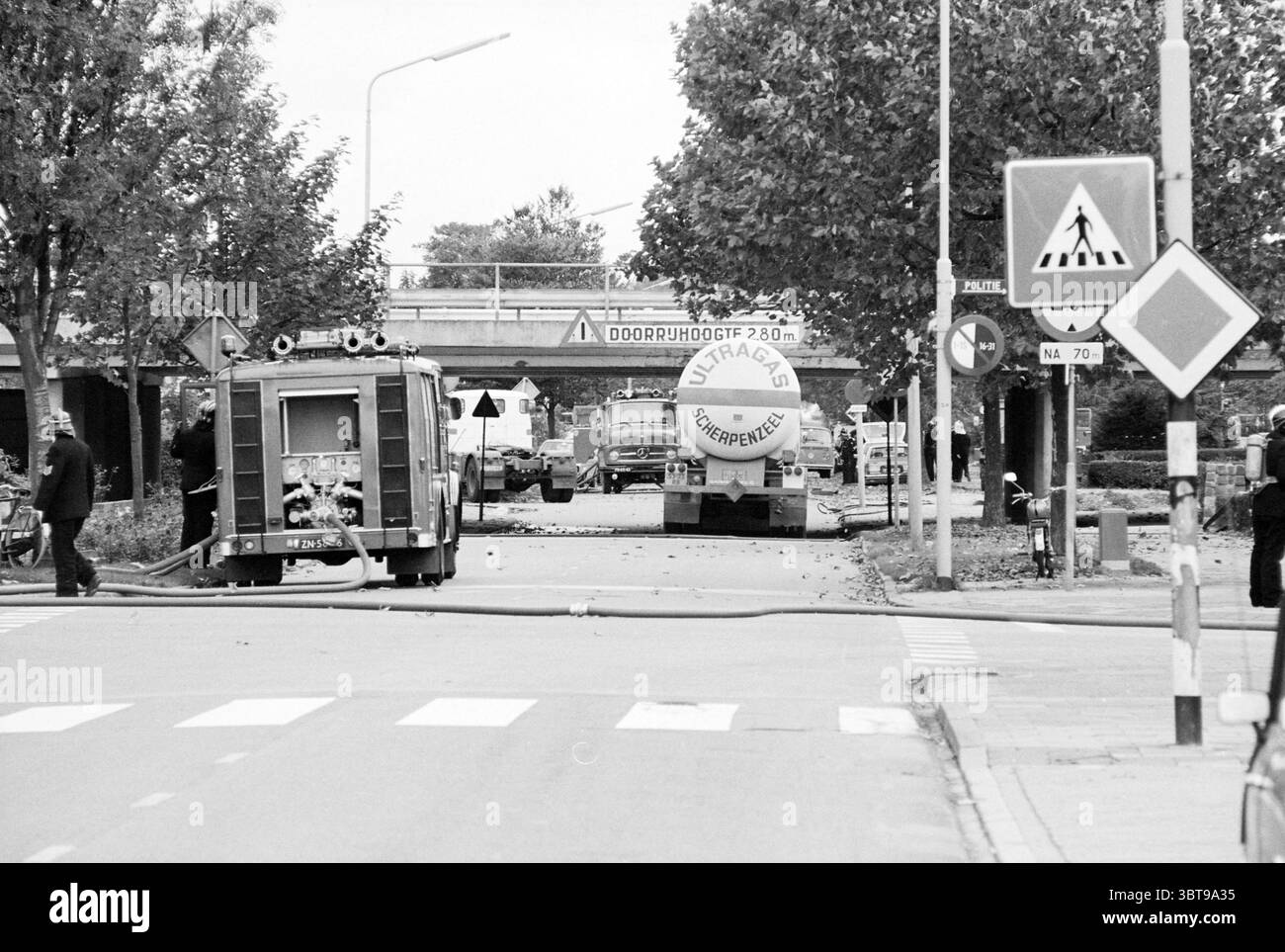 Pompiers sur camion-citerne coincé sous le viaduc de Julianalaan Overveen Julianalaan, Whizgle News, Dutch Desk, pays-Bas, 1950 - 2000 on 16-10-1978. Ces rubriques apparaissent dans l'image. La scène représente un environnement urbain animé capturé en monochrome, présentant un contraste saisissant entre la lumière et l'ombre. Au premier plan, un camion de pompiers, caractérisé par sa conception compacte et divers équipements de lutte contre l'incendie, est stationné avec un tuyau qui s'étend sur le trottoir, laissant entendre une intervention d'urgence continue. Ses surfaces métalliques brillent légèrement sous la lumière disponible. A gauche, un groupe Banque D'Images