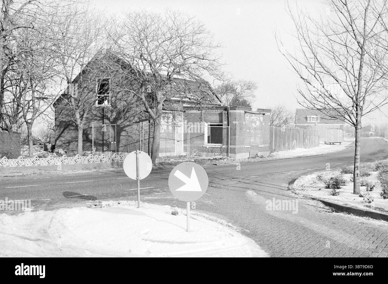 Ext. Salon de coiffure P. Zoet de Zilk coiffeurs et salons de coiffure de Zilk, Whizgle News, Dutch Desk, pays-Bas, 1950 - 2000 on 16-12-1981. L'image montre ces rubriques. La scène représente un paysage calme et hivernal caractérisé par une atmosphère tranquille, presque désolée. Au premier plan, deux panneaux de signalisation circulaires se tiennent bien en évidence à l'intersection, leurs couleurs sourdes contrastant subtilement avec la palette environnante. Un signe pointe vers la droite, tandis que l'autre est vide, ajoutant un élément de simplicité à la composition. Au-delà des panneaux, la route se courbe doucement, conduisant le regard du spectateur vers Banque D'Images