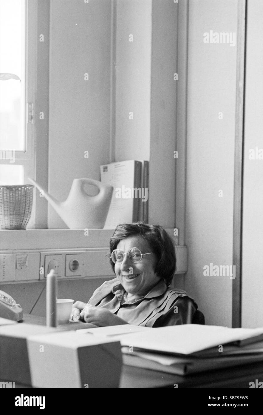 Portrait du Dr Lea Dasberg Université d'Amsterdam Portraits Amsterdam pays-Bas, Whizgle News, Dutch Desk, pays-Bas, 1950 - 2000 le 11-06-1980. L'image montre ces rubriques. Dans une pièce bien éclairée, une femme âgée est assise à un bureau, son comportement chaleureux et accueillant. Elle a les cheveux courts et foncés et porte de grandes lunettes rondes qui accentuent ses yeux expressifs. Ses lèvres se courbent dans un sourire, suggérant un sentiment de joie ou d'amusement. Le réglage propose un mélange de couleurs vives et sourdes. Le fond est orné de murs beiges doux, contribuant à une atmosphère calme. La lumière naturelle pénètre de Banque D'Images