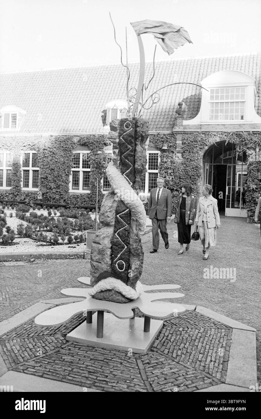 Biennale d'ouverture par CD.K. Musée Frans Hals ouverture ouverture ouverture Haarlem pays-Bas, Whizgle News, Dutch Desk, pays-Bas, 1950 - 2000 le 05-10-1985. Ces rubriques sont illustrées dans l'image. Dans un jardin, une sculpture saisissante attire l'attention, s'élevant d'une base circulaire stylisée qui suggère une fleur. La sculpture présente une combinaison de formes organiques et de lignes abstraites. Il est composé d'un élément vertical central qui ressemble à une grande pierre ou roche, orné d'éléments en métal torsadé et en tissu qui imitent des formes naturelles, telles que des plantes ou des flammes. Le a environnant Banque D'Images