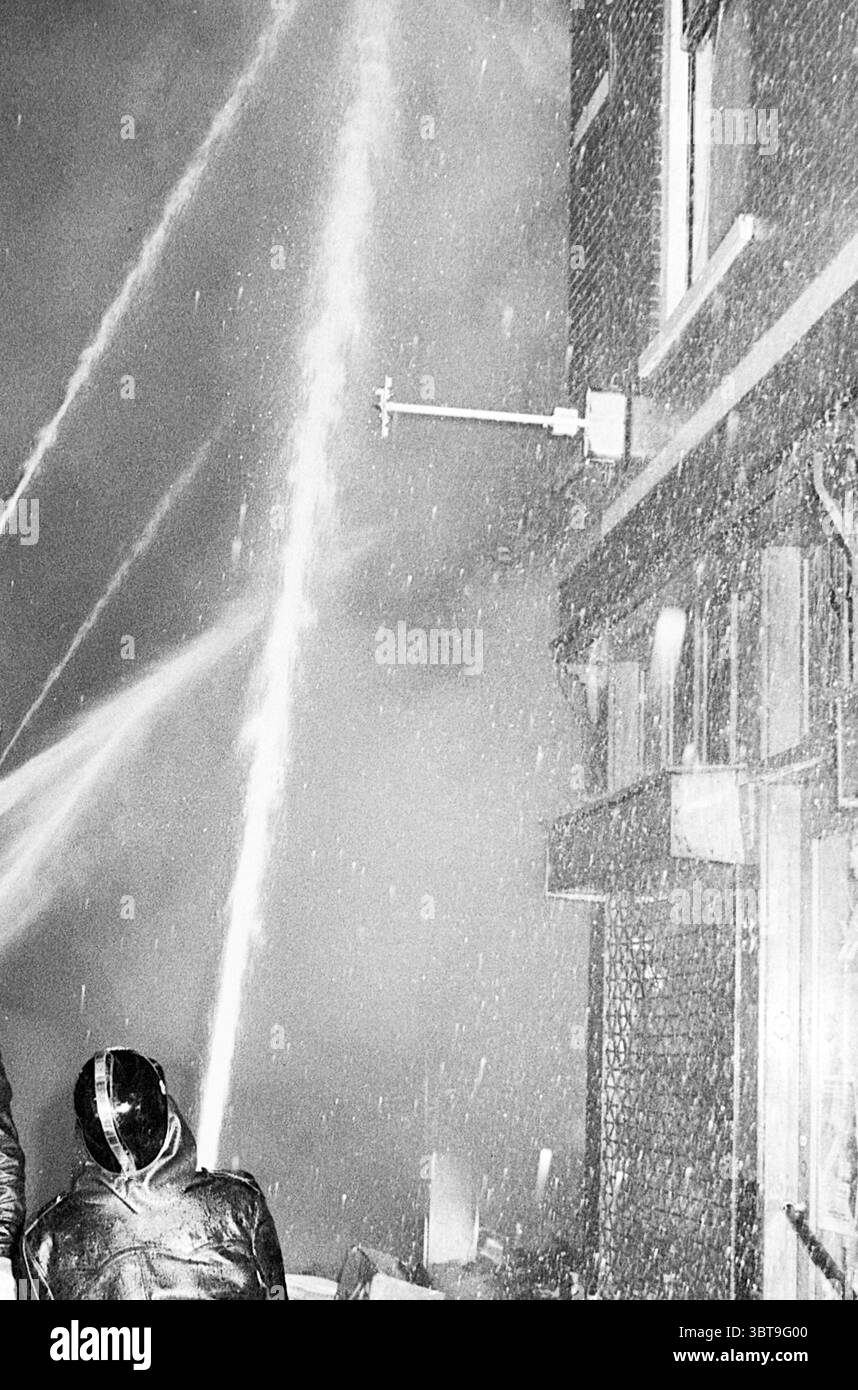 Feu dans le club équestre et Fa. Henssen Haarlem Koningstraat pays-Bas, Whizgle News, Dutch Desk, pays-Bas, 1950 - 2000 le 25-06-1974. L'image inclut ces rubriques. La scène révèle un environnement urbain chaotique englouti dans de fortes chutes de neige, créant un contraste frappant avec les éléments sombres du décor. Un groupe de personnes, vêtues de vêtements sombres, sont positionnées au premier plan, leurs formes partiellement obscurcies par la neige qui tombe. Ils semblent être engagés dans un moment intense, observant peut-être ou réagissant à un événement qui se déroule à proximité. En arrière-plan, un métier à tisser Banque D'Images