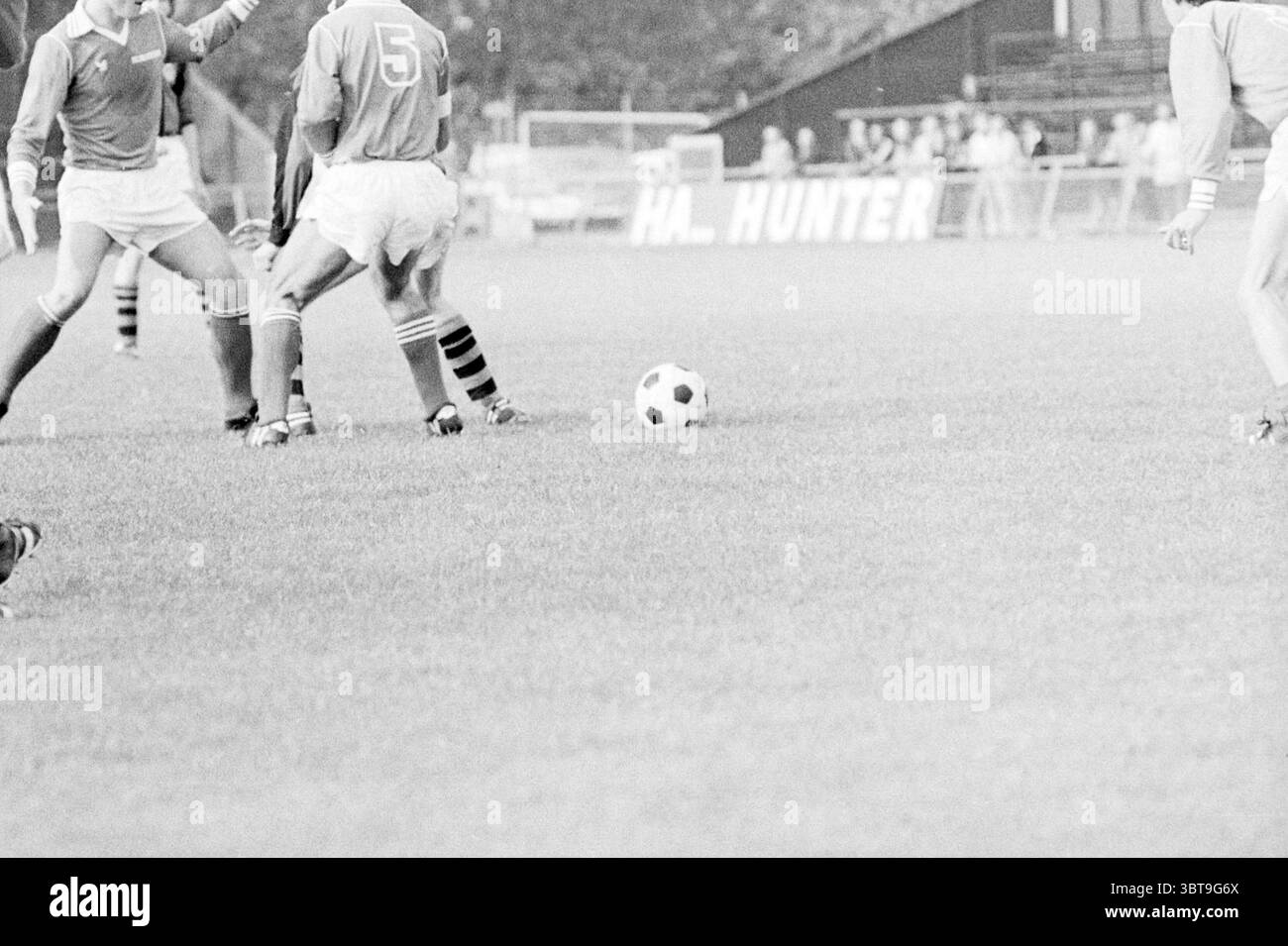 Kennemerland - Energy Football, Whizgle News, Dutch Desk, pays-Bas, 1950 - 2000 le 23-09-1978. L'image montre ces rubriques. La scène se déroule sur un terrain herbeux, vibrant avec les teintes vertes de l'herbe fraîchement coupée. Les joueurs occupent le premier plan, leurs mouvements dynamiques et athlétiques. Deux individus en maillots bleus sont engagés dans un moment tendu, probablement en lice pour la possession d'un ballon de soccer noir et blanc qui repose sur le sol. Les joueurs sont vêtus de shorts, et leurs chaussettes révèlent des rayures contrastées, ajoutant un élément ludique à leur uniformité. Celui de gauche porte le numéro “5” pr Banque D'Images