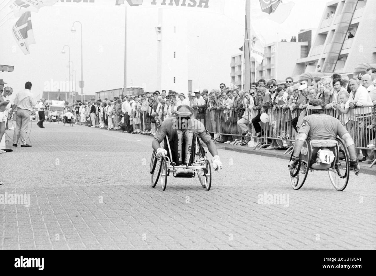 Terminez le marathon en fauteuil roulant à Noordwijk Disabled Sports and Sports week Noordwijk, Whizgle News, Dutch Desk, pays-Bas, 1950 - 2000 on 12-08-1989. L'image montre ces rubriques. Dans une scène dynamique capturant un moment de détermination et de compétition, deux athlètes en fauteuil roulant courent vers une ligne d’arrivée, mettant en valeur leur concentration et leur force. La personne au premier plan a une expression déterminée, portant un uniforme athlétique ajusté qui souligne leur construction musculaire. Leur fauteuil roulant est élégant, conçu pour la vitesse, avec les mains saisissant fermement les poignées, les propulsant vers l'avant avec vis Banque D'Images