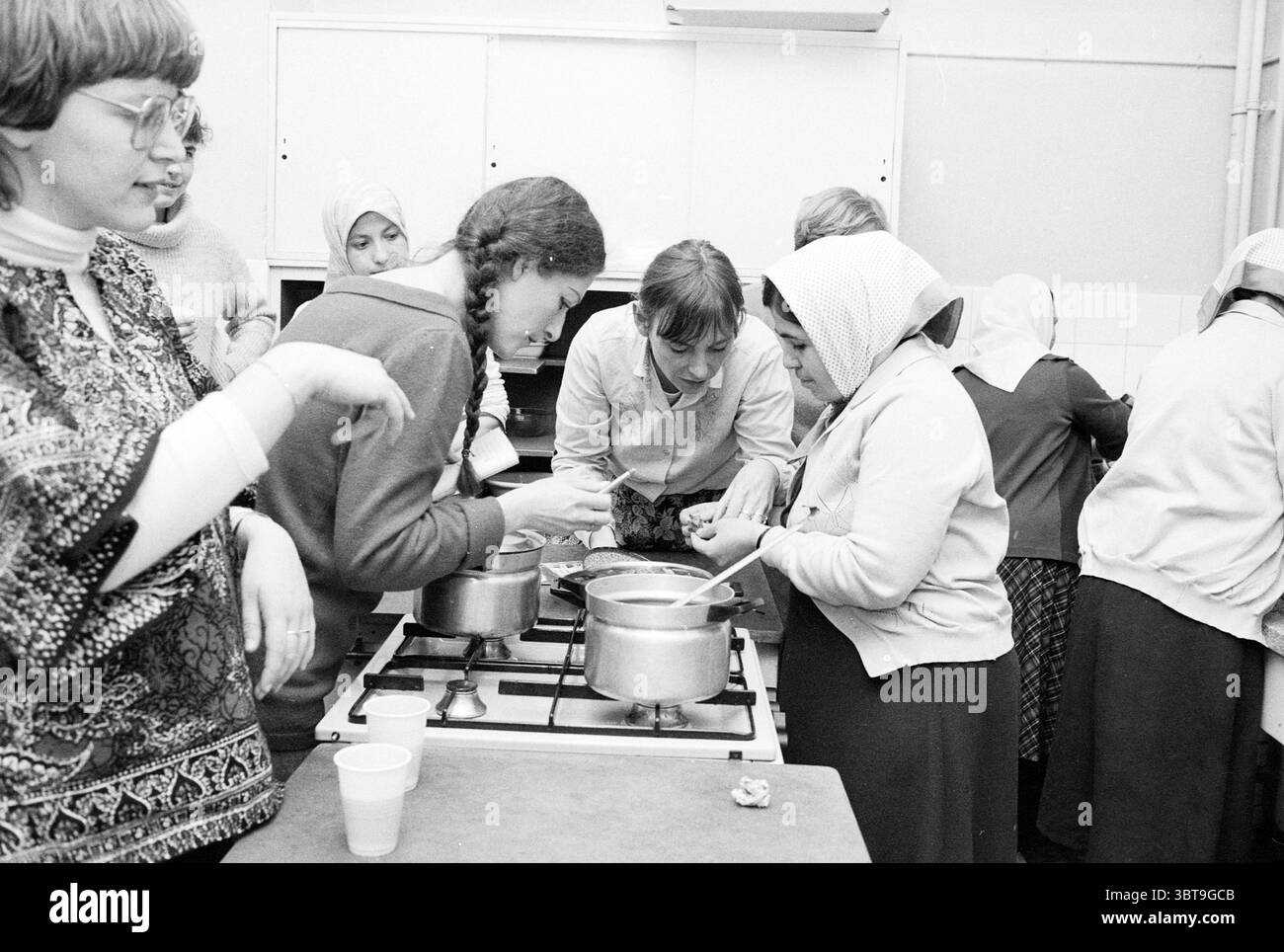 Des femmes turques enseignent la cuisine turque aux femmes néerlandaises, Whizgle News, Dutch Desk, pays-Bas, 1950 - 2000 on 17-01-1983. Ces rubriques sont illustrées dans l'image. La scène se déroule dans une cuisine animée remplie d'activité, caractérisée principalement par un groupe de femmes engagées dans la cuisine commune. L'atmosphère est animée et chaleureuse, avec un sens de la collaboration et un but partagé. Au premier plan, plusieurs femmes sont concentrées sur une cuisinière où deux pots mijotent. Une femme, portant une blouse de couleur claire, se penche étroitement pour examiner le contenu d'un pot, son visage illuminé d'intérêt et co Banque D'Images