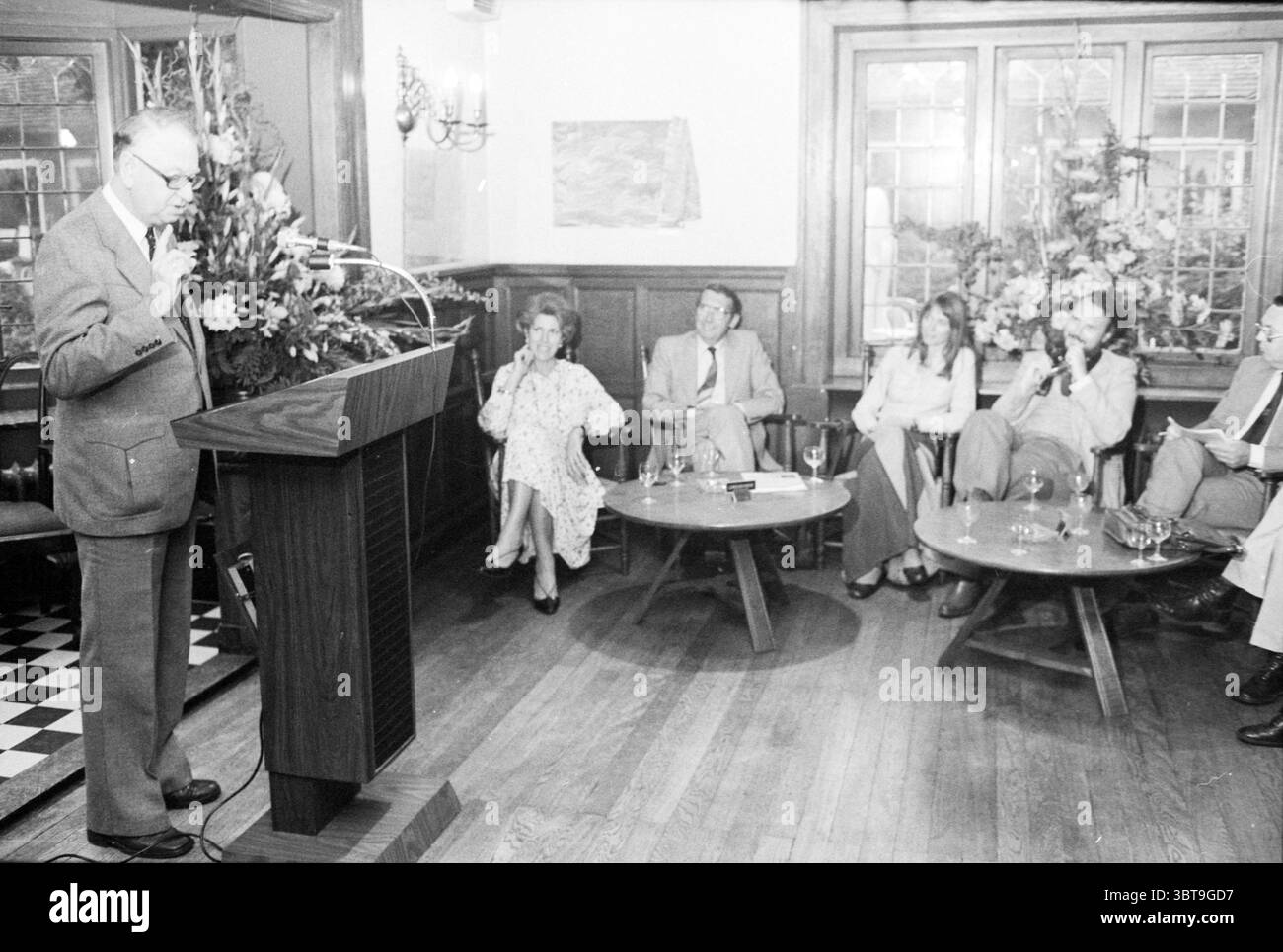 Présentation livre le long de Heeren Roads Laren livres et libraires présentation Spectrum Laren, Whizgle News, Dutch Desk, pays-Bas, 1950 - 2000 le 05-10-1979. L'image contient ces rubriques. Dans un cadre intérieur chaleureusement éclairé caractérisé par des lambris en bois et de grandes fenêtres, un rassemblement est en cours. Un conférencier se tient en toute confiance sur un podium, engageant un public attentif. L'orateur est habillé d'un costume gris formel, avec une expression sérieuse, gestant expressivement alors qu'il partage ses pensées. Assis devant lui, quatre individus sont disposés en demi-cercle autour d'un t circulaire bas Banque D'Images