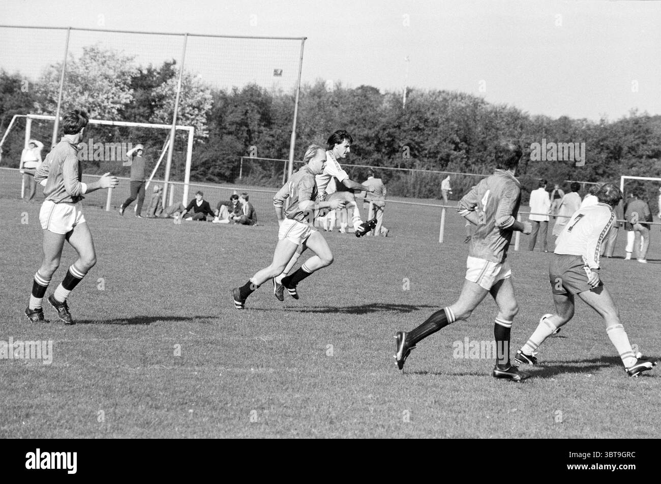 VVB - Waterloo Football VVB, Whizgle News, Dutch Desk, pays-Bas, 1950 - 2000 le 25-09-1983. Ces rubriques apparaissent dans l'image. Dans un cadre extérieur animé, un match de football se déroule sur un terrain verdoyant. L’herbe est bien entretenue, avec une couleur riche et profonde qui contraste avec les uniformes des joueurs. Différentes nuances de gris et de blanc dominent la scène, donnant une sensation classique et désuète, probablement en raison de la présentation monochrome. Plusieurs joueurs sont activement engagés dans le jeu : quelques individus au premier plan font du sprint, leurs corps en mouvement affichant des déterminati Banque D'Images