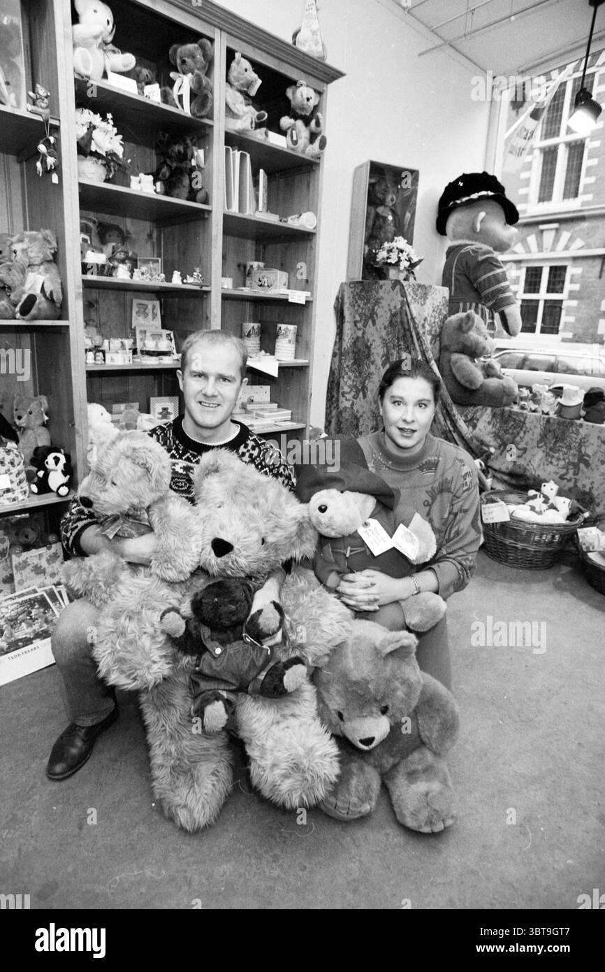 International Bear shop, Whizgle News, Dutch Desk, pays-Bas, 1950 - 2000 sur 08-11-1991. L'image inclut ces rubriques. Dans un cadre intérieur confortable, deux individus sont positionnés au premier plan, entourés d'une délicieuse gamme de jouets en peluche. La scène est remplie d'ours en peluche doux et flous, certains grands et d'autres petits, présentant diverses couleurs comme le brun, le bronzage et la crème. Les ours semblent être bien aimés, avec quelques-uns affichant même des vêtements à l'ancienne. Les individus, un homme et une femme, sont assis sur le sol, tous deux tenant plusieurs ours en peluche, chacun berçant un couple dans leurs bras. L'homme Banque D'Images