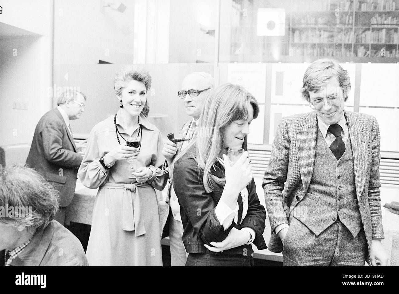 Livre de présentation 100 Years of Modern art Spectrum, Whizgle News, Dutch Desk, pays-Bas, 1950 - 2000 on 26-04-1977. Ces rubriques apparaissent dans l'image. La scène se déroule dans un cadre intérieur animé, probablement lors d'un rassemblement ou d'un événement, caractérisé par un mélange de conversation détendue et d'interaction sociale. Au premier plan, un groupe de quatre individus capte l'attention. Une femme se tient au centre, portant une veste noire élégante, tenant un verre près de sa poitrine. Son expression suggère l’engagement, peut-être écouter attentivement ou partager un moment de lumière. A côté d'elle, une femme glamour avec volu Banque D'Images