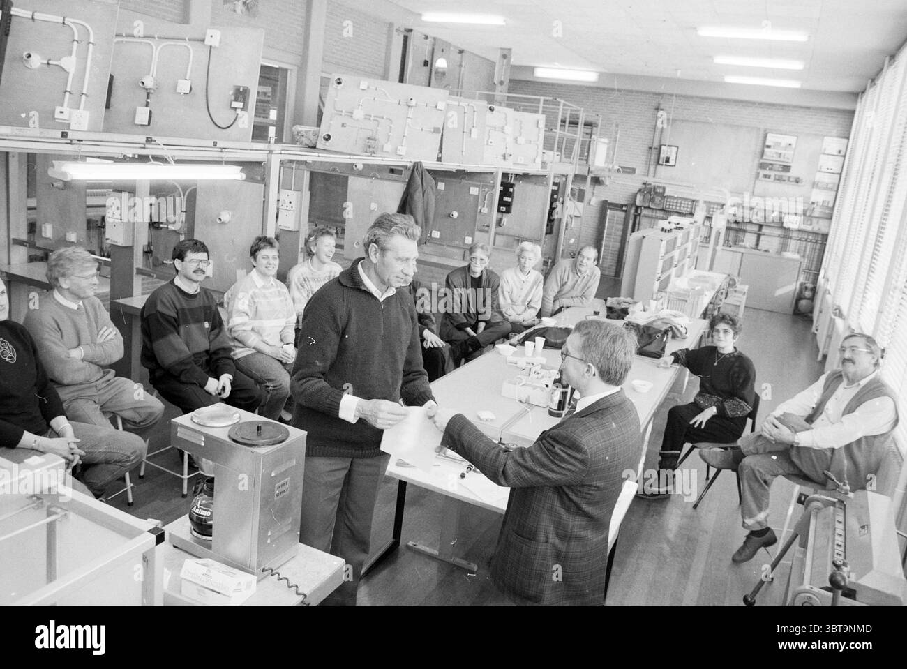 Cérémonie de remise des diplômes Jansoniusschool Hoofddorp Hoofddorp Hoofdweg pays-Bas, Whizgle News, Dutch Desk, pays-Bas, 1950 - 2000 on 08-02-1991. Ces rubriques sont illustrées dans l'image. Dans une pièce spacieuse éclairée par une lumière douce et naturelle filtrant à travers de grandes fenêtres, un groupe diversifié de personnes est réuni autour d'une longue table. Le cadre semble être un atelier ou une salle de classe rempli de divers équipements et matériels techniques visibles en arrière-plan, suggérant un environnement d'apprentissage pratique. Assis à la table sont plusieurs personnes, hommes et femmes, qui présentent une gamme de Banque D'Images