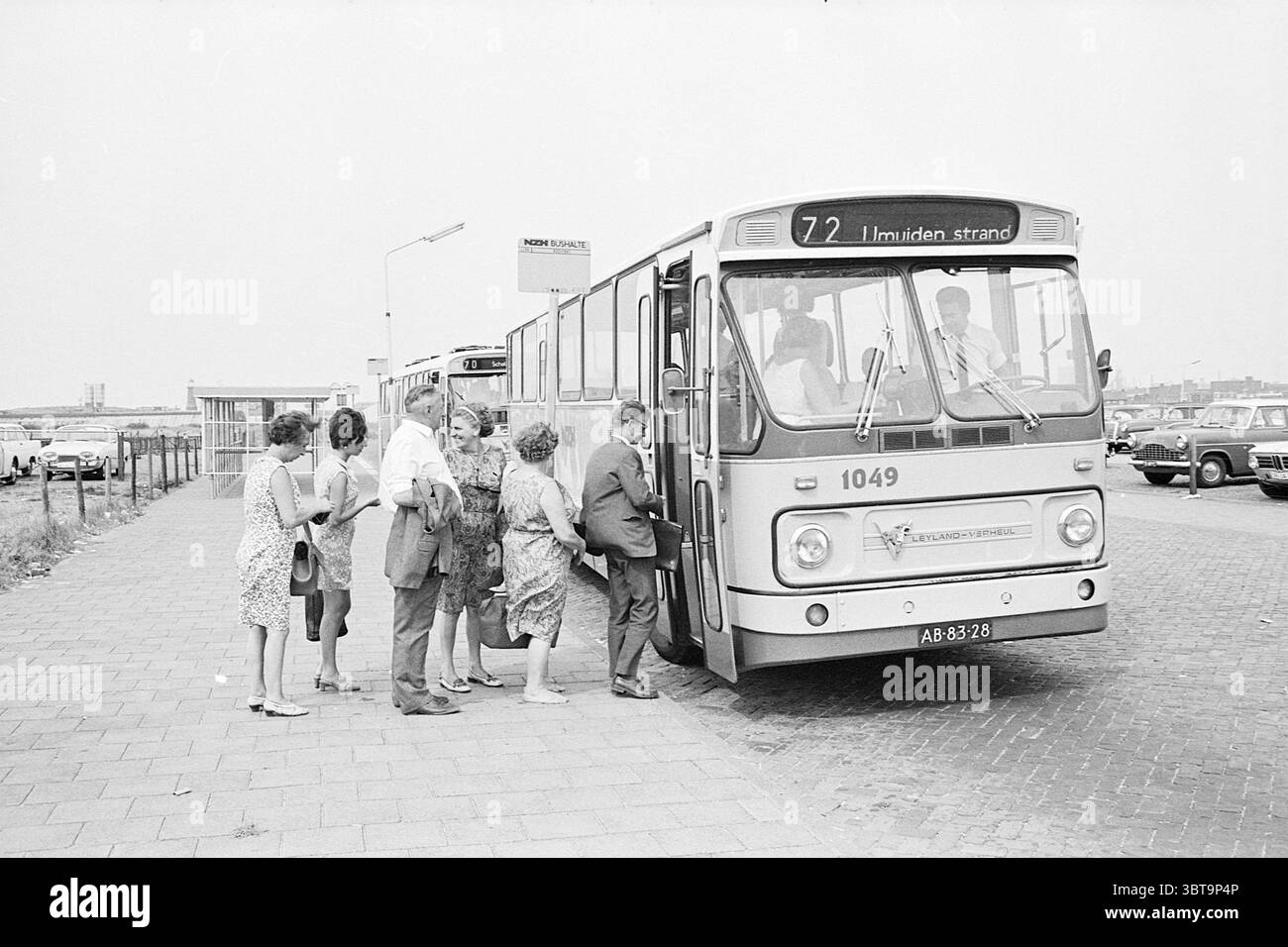 Bus sur Boulevard Noord Zuid Hollandse Vervoersmaatschappij N.V. NZ, Whizgle News, Dutch Desk, pays-Bas, 1950 - 2000 on 12-08-1969. L'image contient ces rubriques. La scène représente un groupe de personnes rassemblées à un arrêt de bus, avec plusieurs individus se dirigeant vers un bus. Le bus, doté d'un devant proéminent et de grandes fenêtres, affiche un numéro d'itinéraire sur le pare-brise. Son extérieur est marqué par un design classique, affichant une couleur claire qui contraste avec son environnement. Les personnes qui attendent paraissent diverses, avec un mélange de sexes et d'âges. Certains individus sont habillés en somme décontractée Banque D'Images