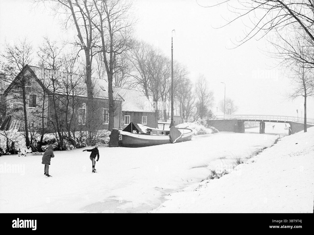 Skating photos Leidsevaart Skating Haarlem Leidsevaart pays-Bas, Whizgle News, Dutch Desk, pays-Bas, 1950 - 2000 on 23-12-1981. Voici les rubriques de l'image. Une scène hivernale sereine se déroule, caractérisée par une couverture de neige blanche qui couvre le sol et couvre le paysage. L'atmosphère est imprégnée d'une lumière douce et silencieuse, suggérant un ciel couvert ou de légères chutes de neige, donnant à tout une qualité légèrement éthérée. Des bruits de brouillard planent au-dessus de la glace, améliorant l'ambiance tranquille. Au premier plan, deux figures glissent gracieusement sur la surface gelée d'un canal. Ils Ar Banque D'Images