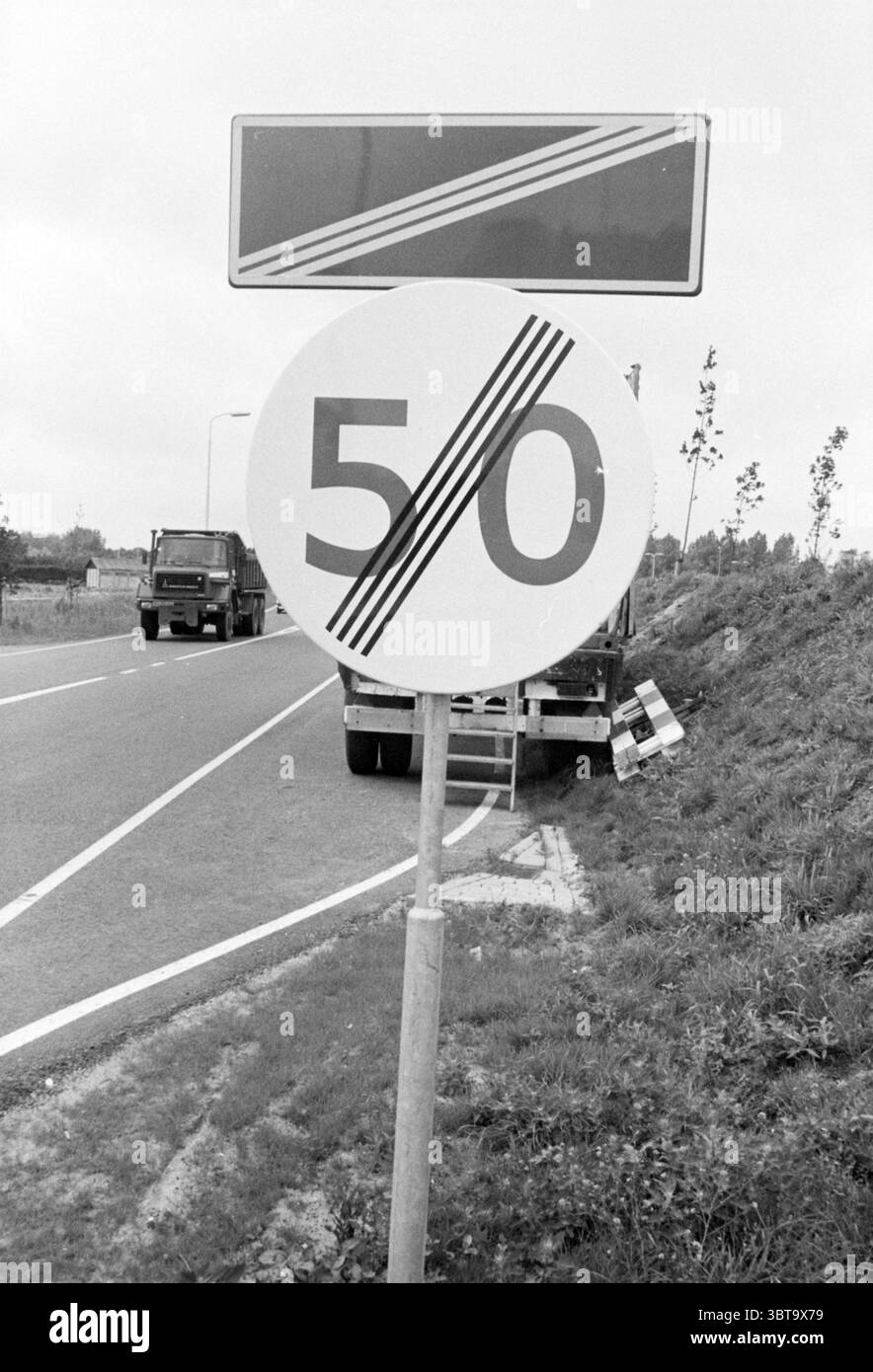 50 km panneau lisse Borden lisse, Whizgle News, Dutch Desk, pays-Bas, 1950 - 2000 sur 16-07-1984. L'image inclut ces rubriques. La scène représente une route avec un panneau circulaire proéminent debout à côté. Le signe affiche un chiffre en gras '50' dans une grande police de caractères, avec trois lignes diagonales qui le traversent, suggérant une limite de vitesse. Le fond du panneau est principalement blanc, et il est entouré d'une épaisse bordure noire, améliorant sa visibilité dans les environs. À gauche du panneau, une partie de la chaussée est visible, bordée d'un étroit séparateur marqué par w faible Banque D'Images