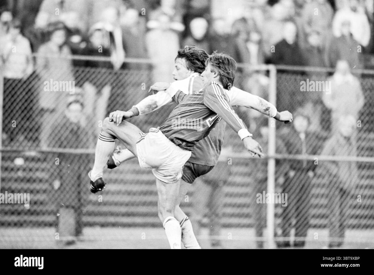 Telstar - NVV Football Telstar, Whizgle News, Dutch Desk, pays-Bas, 1950 - 2000 on 28-11-1982. L'image contient ces rubriques. La scène capture un moment intense dans un match de football. Deux joueurs sont engagés dans une lutte acharnée, l'un aéroporté avec les jambes tendues et l'autre essayant de maintenir l'équilibre, créant une tension dynamique dans la composition. Le joueur aéroporté porte un maillot blanc, tandis que l'autre porte un uniforme plus foncé, peut-être rouge ou marron. Leurs expressions véhiculent la détermination et l'effort. Le fond est rempli d'un public, leurs visages quelque peu flous mais indicat Banque D'Images