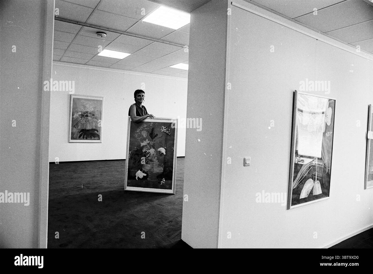 Création de SBK Jaspers, Whizgle News, Dutch Desk, pays-Bas, 1950 - 2000 le 31-07-1995. L'image contient ces rubriques. La scène dispose d'une galerie d'art spacieuse caractérisée par ses murs blancs et un tapis aux tons doux qui ajoute une sensation de chaleur à l'environnement autrement minimaliste. L'éclairage est lumineux et uniforme, émanant de luminaires suspendus qui éclairent l'espace sans ombres dures, créant une atmosphère accueillante et ouverte. Au centre de la scène, une personne se tient juste à l'extérieur du cadre de la porte, visible seulement de la taille vers le haut. Cette personne est engagée dans un moment de publicité Banque D'Images