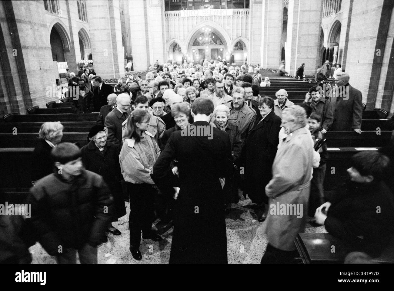 Les personnes saluent le prêtre dans la cathédrale de Bavo Leidsevaart Haarlem pays-Bas, Whizgle News, Dutch Desk, pays-Bas, 1950 - 2000 le 28-03-1992. Ces rubriques apparaissent dans l'image. La scène représente un rassemblement animé dans un grand espace architectural, caractérisé par des colonnes de pierre et des arches complexes qui créent un sentiment de majesté. L'intérieur est baigné d'une lumière douce et diffuse filtrant à travers de hautes fenêtres, projetant de douces ombres sur le sol poli. Au premier plan, un groupe de personnes interagit de manière animée. Ils sont disposés en demi-cercle autour d'un homme habillé en f Banque D'Images