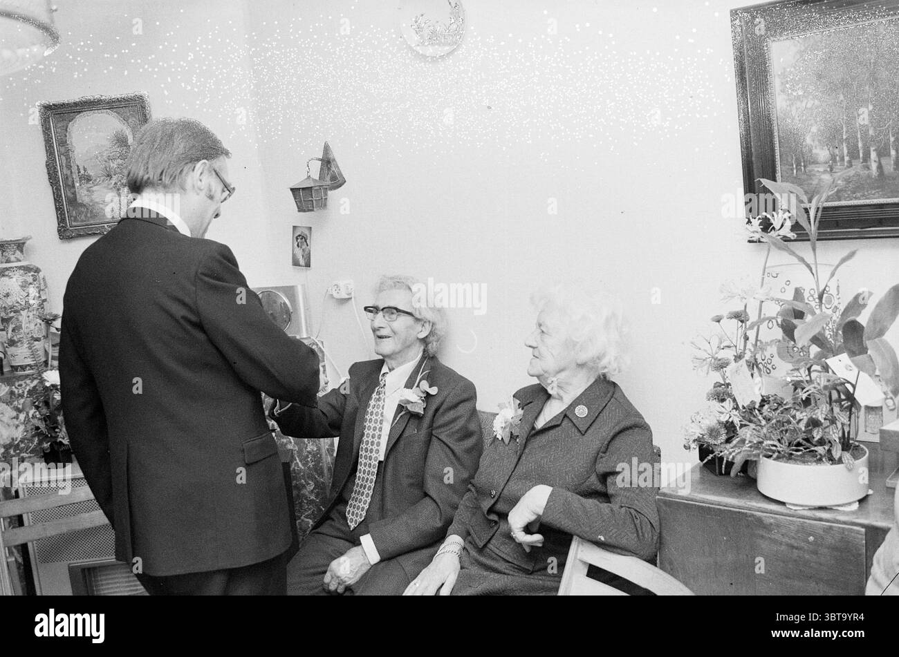 Couple de mariés Lions personnes mariées, Whizgle News, Dutch Desk, pays-Bas, 1950 - 2000 sur 11-12-1973. Ces rubriques apparaissent dans l'image. Dans un cadre intérieur confortable, deux femmes âgées s'assoient étroitement ensemble, toutes deux habillées élégamment. Une femme porte un blazer foncé avec un col élégant, tandis que l'autre, arborant un ensemble de couleur plus claire, a des cheveux blancs tortueux encadrant son visage. Leurs expressions reflètent la chaleur et le contentement lorsqu'ils s'engagent dans la conversation. Un gentleman se tient à proximité, vêtu d'un costume formel, avec un comportement ludique mais respectueux. Il semble interagir avec les femmes, Banque D'Images