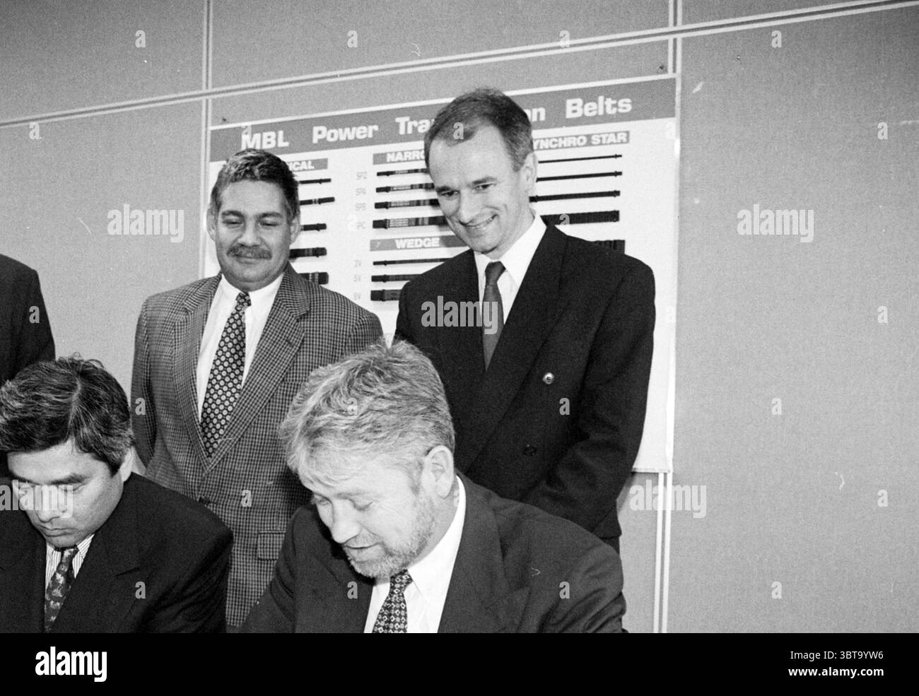 Signer contrat MLB - Bestmate [Major League Baseball], Whizgle News, Dutch Desk, pays-Bas, 1950 - 2000 le 12-09-1996. Ces rubriques sont illustrées dans l'image. La scène représente un cadre intérieur formel, probablement un environnement corporatif ou organisationnel. Au premier plan, trois hommes sont assis à une table, avec un homme en costume gris signant visiblement des documents. Son expression transmet la concentration et le sérieux alors qu'il se penche en avant, plume à la main. À sa gauche, un autre homme, vêtu d'un costume sombre, semble également engagé dans le processus mais regarde vers le bas, suggérant concentration ou contemplation. Sur la droite, Banque D'Images