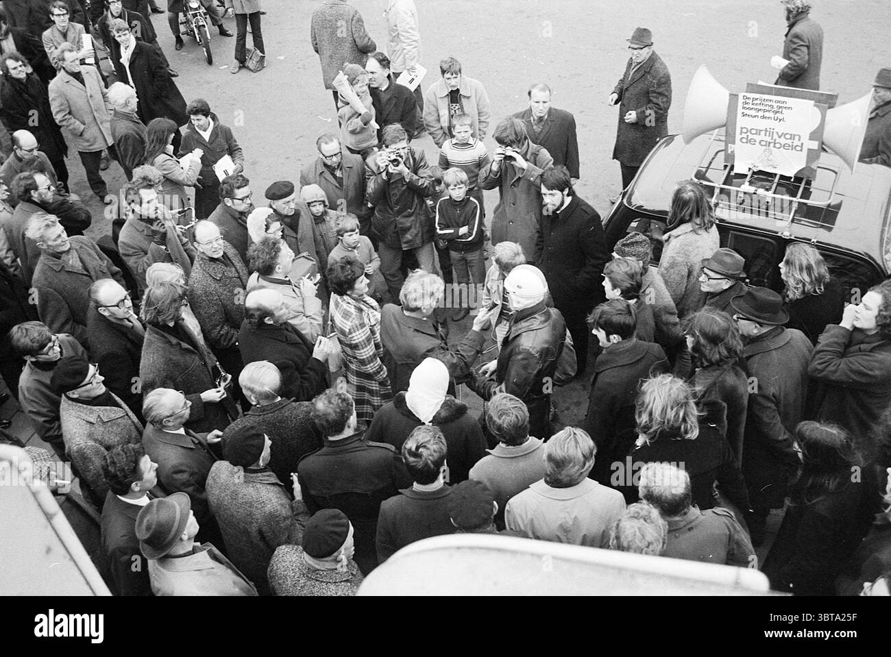 Campagne électorale DU PVDA dans les rues, Whizgle News, Dutch Desk, pays-Bas, 1950 - 2000 on 03-1971. Ces rubriques apparaissent dans l'image. La scène capture un rassemblement urbain animé, avec une foule diversifiée densément emballée autour d'une figure centrale. De nombreuses personnes sont habillées dans des vêtements des années 1960 ou 70, avec des manteaux longs, des chapeaux et des foulards, qui créent un visuel texturé de tissu et de style. Les expressions de la foule vont de la curiosité à la ferveur, indiquant un fort engagement émotionnel avec l'événement. Au premier plan, un homme parle passionnément, faisant des gestes animés alors qu'il s'adresse au A. Banque D'Images