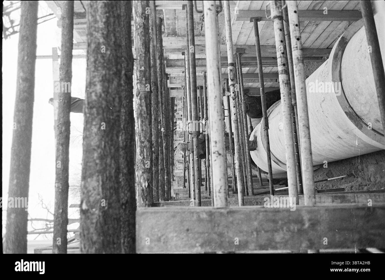 Ouvrages d'assainissement Parklaan Works Haarlem Parklaan pays-Bas, Whizgle News, Dutch Desk, pays-Bas, 1950 - 2000 on 15-12-1965. Ce sont les éléments de l'image. La scène capture un chantier de construction caractérisé par une esthétique brutale et utilitaire. Les poutres en bois verticales sont hautes, formant un cadre squelettique qui fait allusion à la structure émergente. Ces poutres sont entrecoupées d'échafaudages métalliques, créant un motif en forme de grille qui attire l'œil vers le haut. Au premier plan, un grand objet cylindrique, éventuellement une bétonnière ou un conteneur de stockage, occupe une position proéminente. Banque D'Images