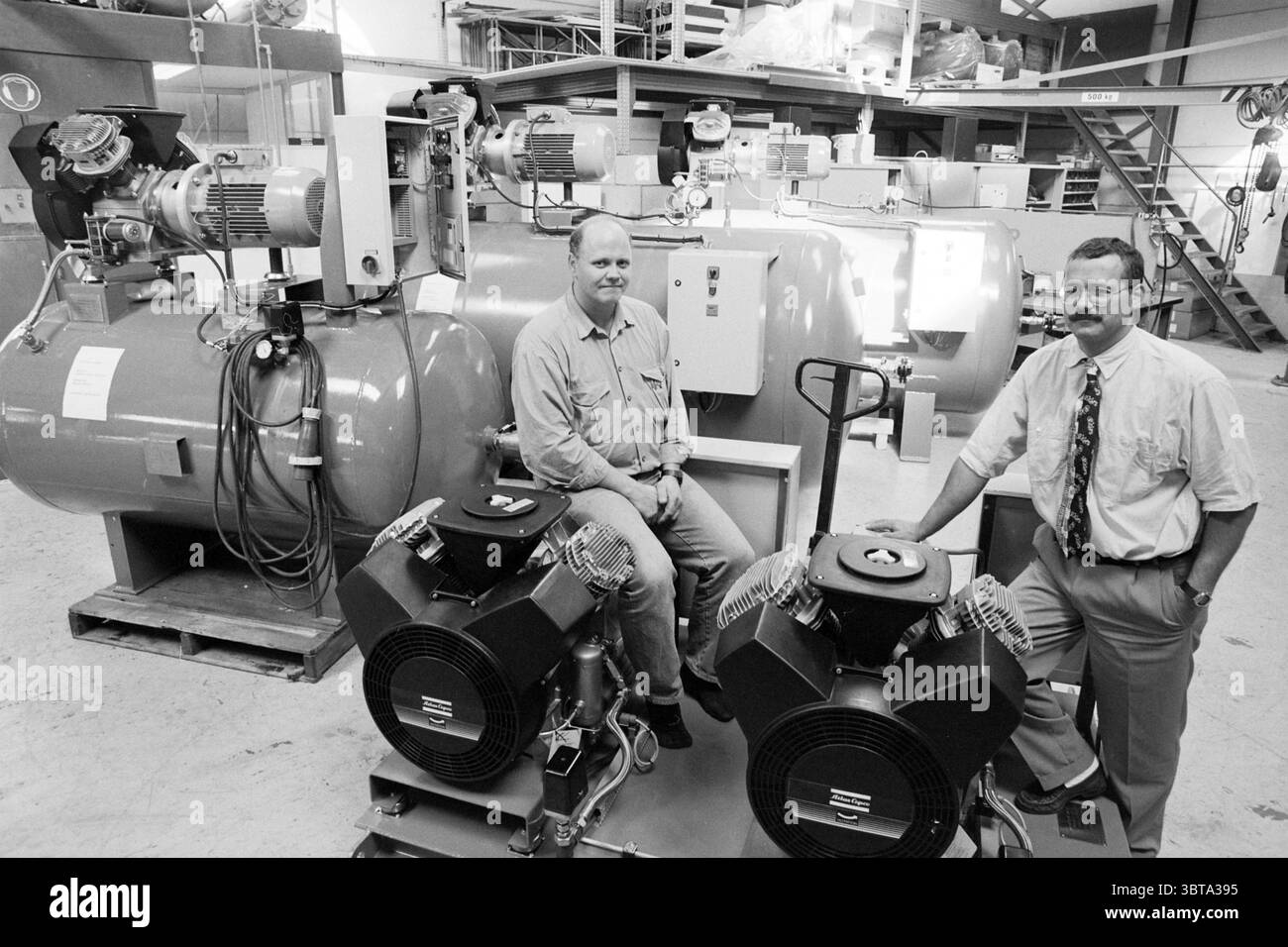 Mr. vis Ketting IJm. IJmuiden pays-Bas, Whizgle News, Dutch Desk, pays-Bas, 1950 - 2000 le 08-09-1996. L'image montre ces rubriques. La scène dispose d'un cadre industriel spacieux, caractérisé par une gamme de grandes machines et équipements. Au centre de la composition se trouvent deux hommes positionnés en bonne place parmi les machines robustes. Un homme s'assoit décontracté sur une unité de compresseur de grande taille, portant une chemise de couleur claire avec des manches roulées, exsudant un comportement détendu. L'autre homme se tient confiant à côté d'un autre compresseur, vêtu d'une chemise et d'une cravate plus formelles, dépeignant une profession Banque D'Images