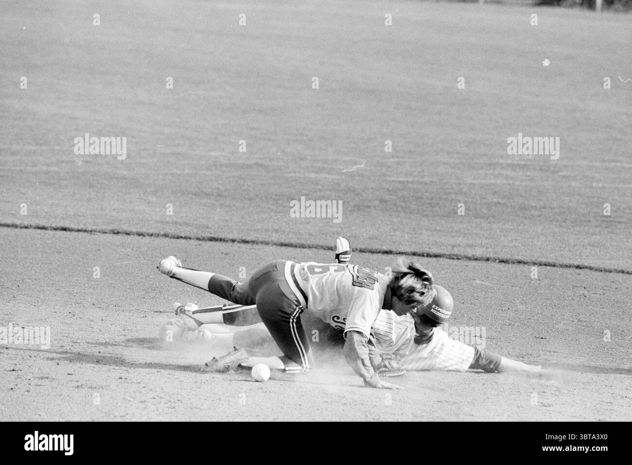 Softball Sparks - Terrasvogels, Whizgle News, Dutch Desk, pays-Bas, 1950 - 2000 on 10-06-1994. Voici les rubriques de l'image. La scène capture l'intensité d'un match de baseball, en se concentrant sur deux joueurs au milieu d'un jeu dynamique. Un joueur, vêtu d'un uniforme rayé, glisse vers une base, avec son corps bas au sol, créant un nuage de poussière autour de lui. Son expression est une expression de détermination lorsqu'il tend la main, peut-être en essayant d'éviter une étiquette. L'autre joueur, portant un maillot avec un numéro affiché en évidence dans le dos, est étendu sur le sol, ayant jus Banque D'Images