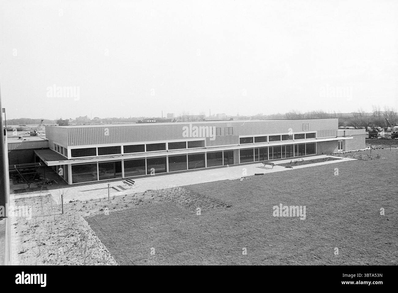 Report Motel Oestgeest Noord Zuid Hollandse Vervoersmaatschappij N.V. NZ Report, Whizgle News, Dutch Desk, pays-Bas, 1950 - 2000 on 18-03-1968. Ce sont les éléments de l'image. La scène présente une structure architecturale moderne contre un paysage serein et expansif. Le bâtiment présente un design minimaliste, caractérisé par de grandes fenêtres rectangulaires qui s'étendent sur toute sa longueur, permettant à une abondance de lumière naturelle d'inonder l'intérieur. La façade extérieure semble être une combinaison de béton et de métal, présentant des lignes épurées et une esthétique fonctionnelle. Entourant la structure Banque D'Images