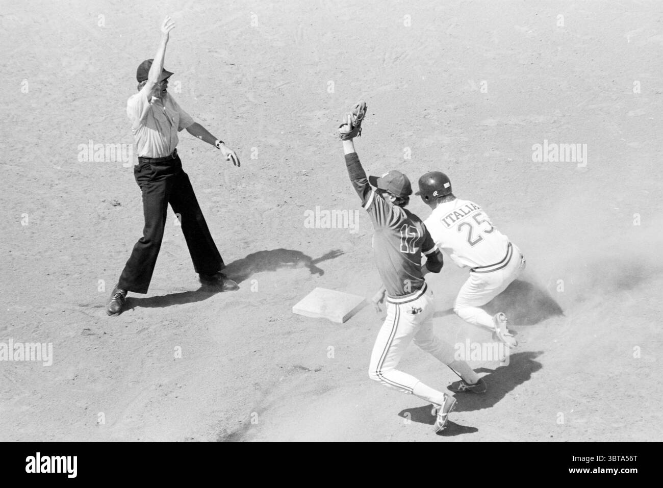 Pays-Bas - Italie (Sat) Baseball, Whizgle News, Dutch Desk, pays-Bas, 1950 - 2000 le 13-07-1985. Voici les rubriques de l'image. La scène capture un moment intense sur un terrain de baseball, où deux joueurs sont en mouvement dynamique. Un athlète, vêtu d'un maillot sombre aux couleurs vives et d'une casquette, est positionné près d'une base, tendre la main avec un gant pour attraper une balle qui semble voler dans les airs. Sa posture suggère de la détermination, avec ses jambes légèrement pliées et ses muscles tendus. Le deuxième joueur, portant un maillot plus léger orné d'un numéro proéminent, glisse en t Banque D'Images