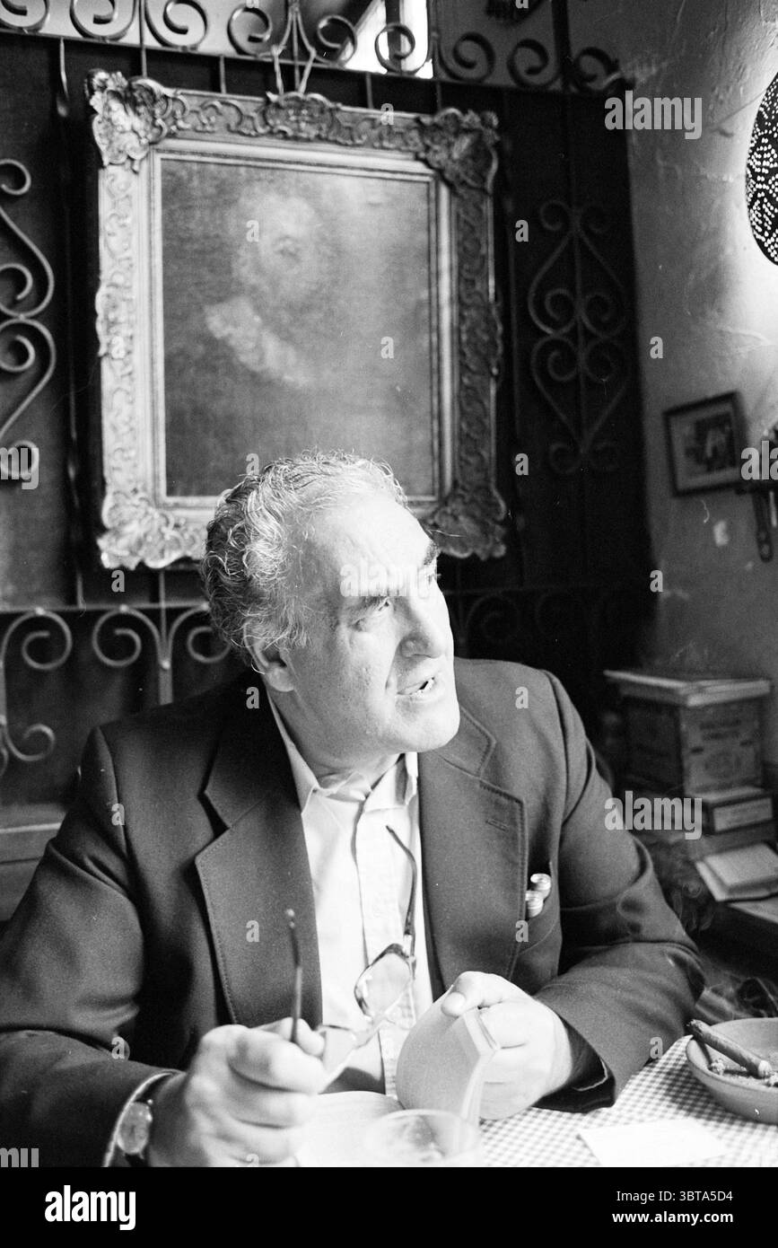 Rapport le plus sec Tourisme touristes Diest België, Whizgle News, Dutch Desk, pays-Bas, 1950 - 2000 sur 20-05-1980. Ces rubriques apparaissent dans l'image. Un gentleman est assis sur une nappe rustique à carreaux, entouré d'un cadre chaleureux et intime. Il a les cheveux grisonnés et une expression réfléchie, avec son regard dirigé vers le haut comme s'il réfléchissait à quelque chose de profond. Vêtu d'un blazer foncé, il tient un petit objet dans une main tandis que l'autre berce une paire de lunettes. L'arrière-plan révèle un mur orné d'un cadre vintage orné qui abrite un portrait légèrement éclairé, contribuant à la nosta de la pièce Banque D'Images