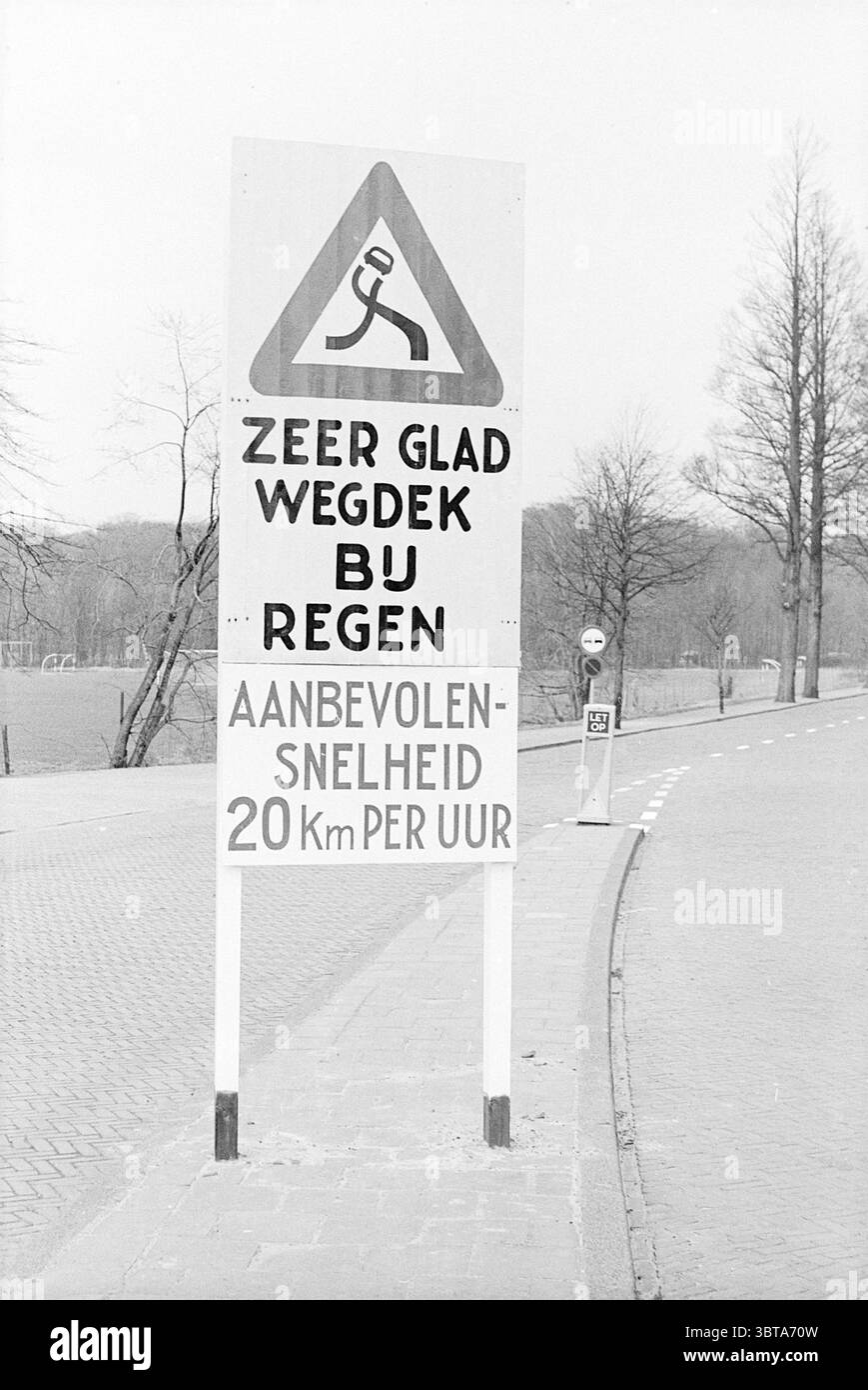 Panneau '20 km' Heemstede Signs, Whizgle News, Dutch Desk, pays-Bas, 1950 - 2000 le 13-03-1968. L'image contient ces rubriques. La scène présente un grand panneau debout bien en vue à côté d'une route. Le panneau est conçu pour transmettre des informations importantes, avec une forme de mise en garde triangulaire en haut, soulignée par un fond jaune. À l’intérieur du triangle, il y a une silhouette noire qui suggère de la prudence ou de la vigilance, représentant probablement une personne glissant. La partie inférieure du panneau fournit des détails supplémentaires dans un format clair et gras, mettant l'accent sur les conditions glissantes, en particulier lorsque Banque D'Images