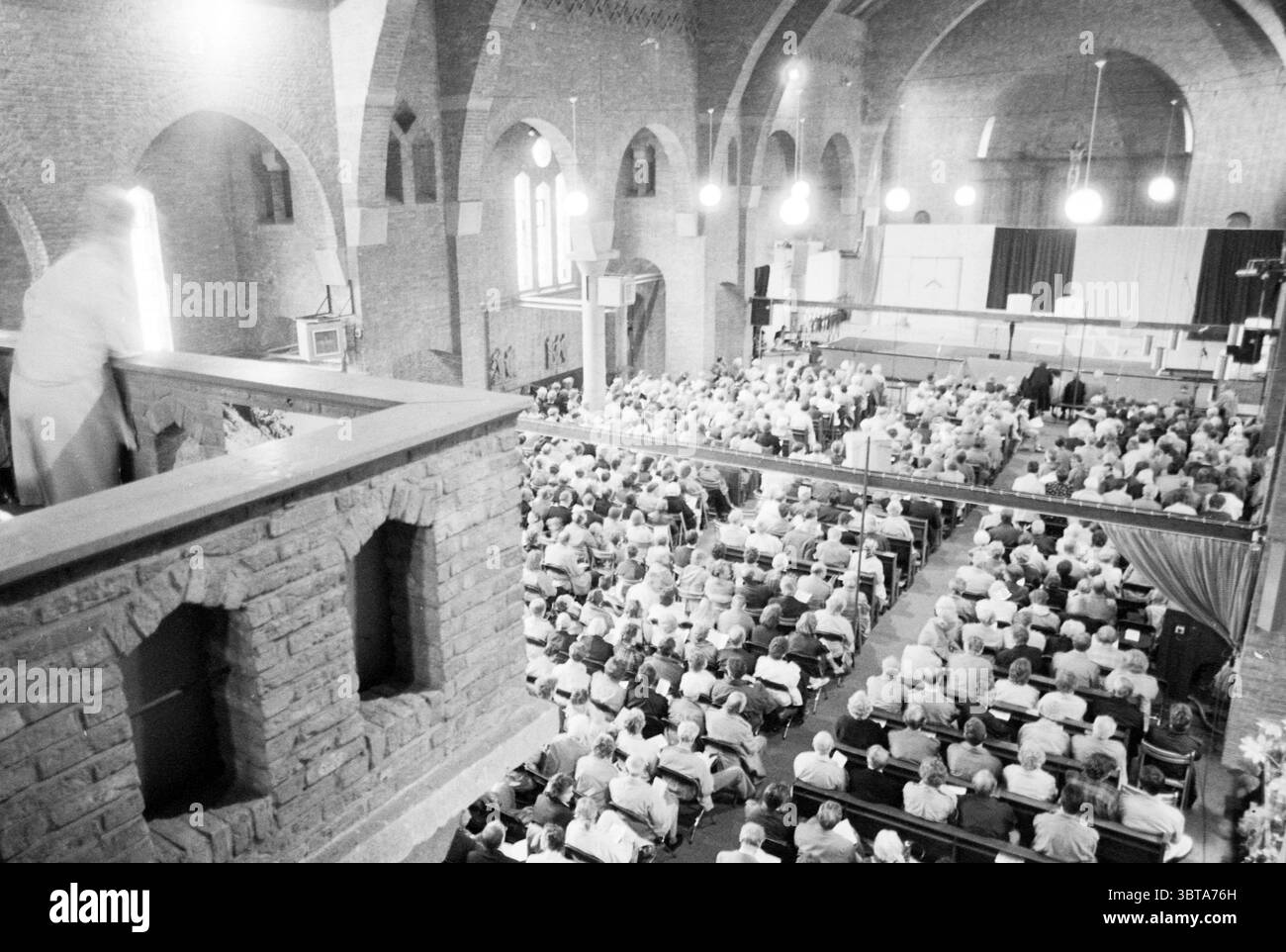 Rencontre œcuménique de Pentecôte dans l'ancienne église de la très Sainte Trinité Bloemendaal Korte Kleverlaan 1, Whizgle News, Dutch Desk, pays-Bas, 1950 - 2000 on 07-06-1987. Ces rubriques sont illustrées dans l'image. La scène capture un grand rassemblement dans un grand espace intérieur, caractérisé par de hauts plafonds voûtés et une série de grandes fenêtres qui permettent à une lumière chaude et naturelle de filtrer, améliorant l'atmosphère globale. Les caractéristiques architecturales du bâtiment sont proéminentes, avec des murs de briques qui ajoutent une sensation de chaleur et d'intemporalité à l'environnement. La foule est densément tassée, composée Banque D'Images