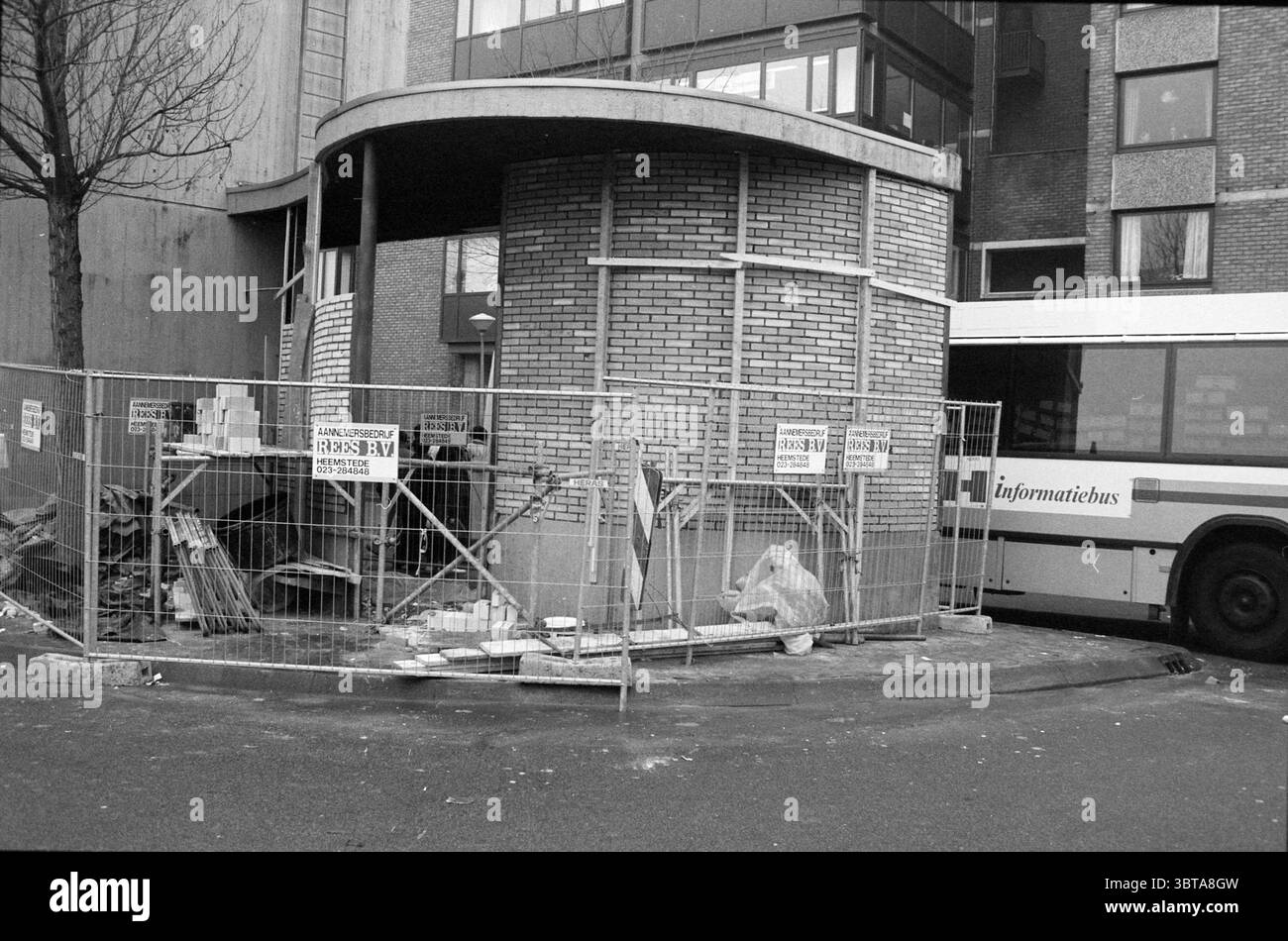 Rénovation de la gare routière H'lem Haarlem pays-Bas, Whizgle News, Dutch Desk, pays-Bas, 1950 - 2000 le 15-12-1991. L'image contient ces rubriques. La scène présente un chantier de construction partiellement clos par une clôture métallique, créant un sentiment de travail en cours. La clôture, ornée de panneaux d'avertissement, ajoute une couche de prudence au cadre. Des briques empilées, des débris dispersés et des matériaux de construction sont éparpillés sur le sol, suggérant un projet de rénovation ou de construction en cours. Au premier plan, une structure circulaire faite de briques se tient en évidence, sa texture riche en Banque D'Images