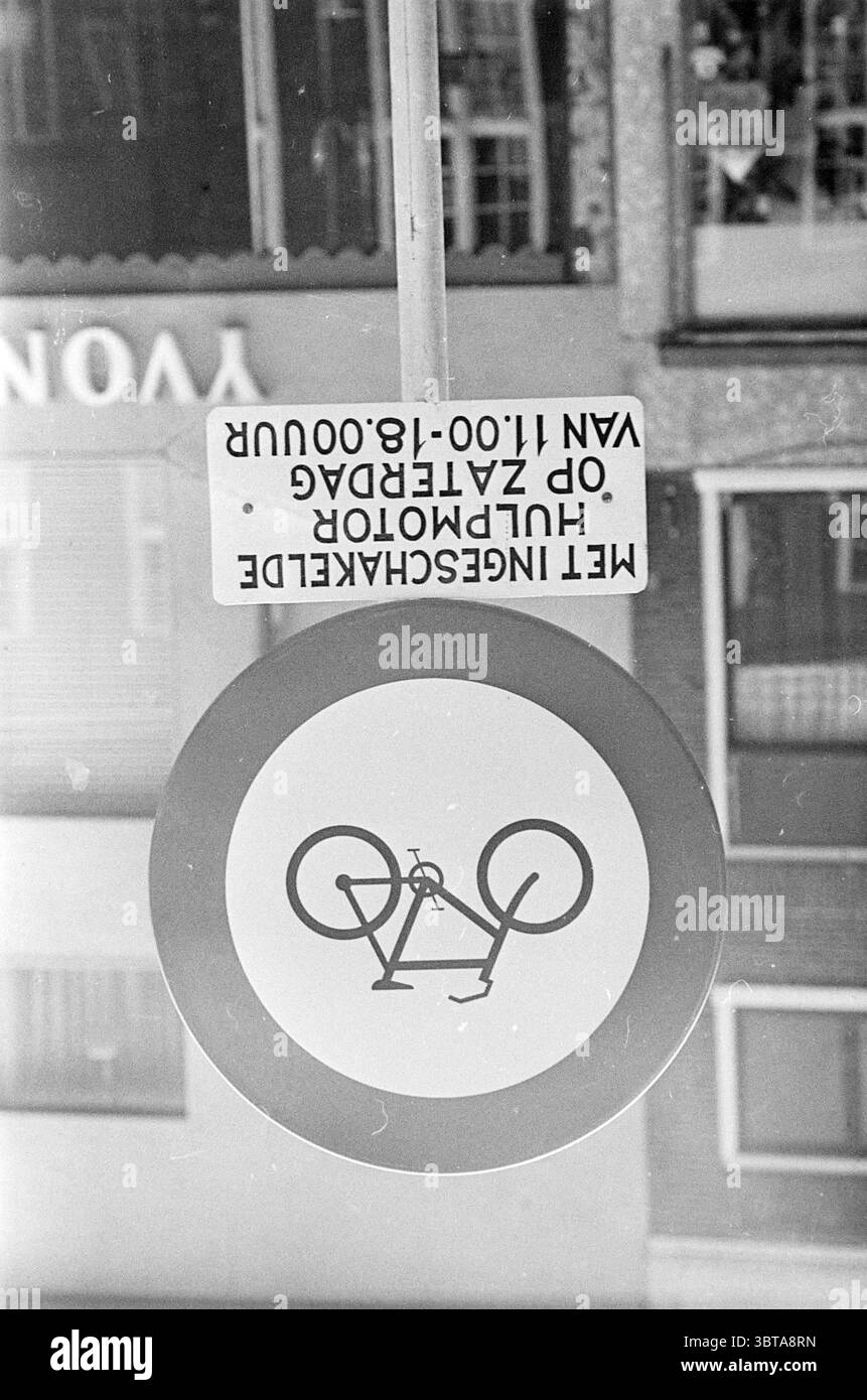 Pancarte d'interdiction d'entrée pour les panneaux de cyclomoteurs, Whizgle News, Dutch Desk, pays-Bas, 1950 - 2000 le 04-07-1966. L'image inclut ces rubriques. La scène présente un panneau de signalisation circulaire mis en évidence sur un fond contrasté. Le panneau présente un design simpliste avec un motif de vélo stylisé, rendu dans un style épuré et moderne. La couleur principale du panneau est le blanc, qui met en évidence la silhouette d'un vélo, probablement peint en noir ou dans une teinte plus foncée. Autour du panneau se trouve un environnement urbain important, évoqué par les détails des structures voisines et des surfaces réfléchissantes. Banque D'Images